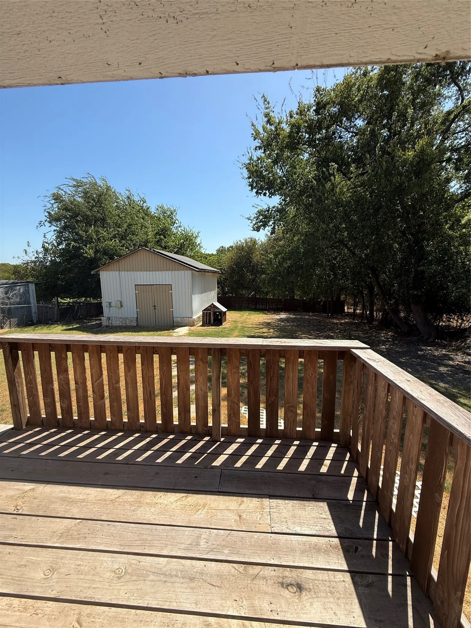 Expansive wood deck with a full wood railing overlooking a grassy yard with mature trees and a detached storage shed