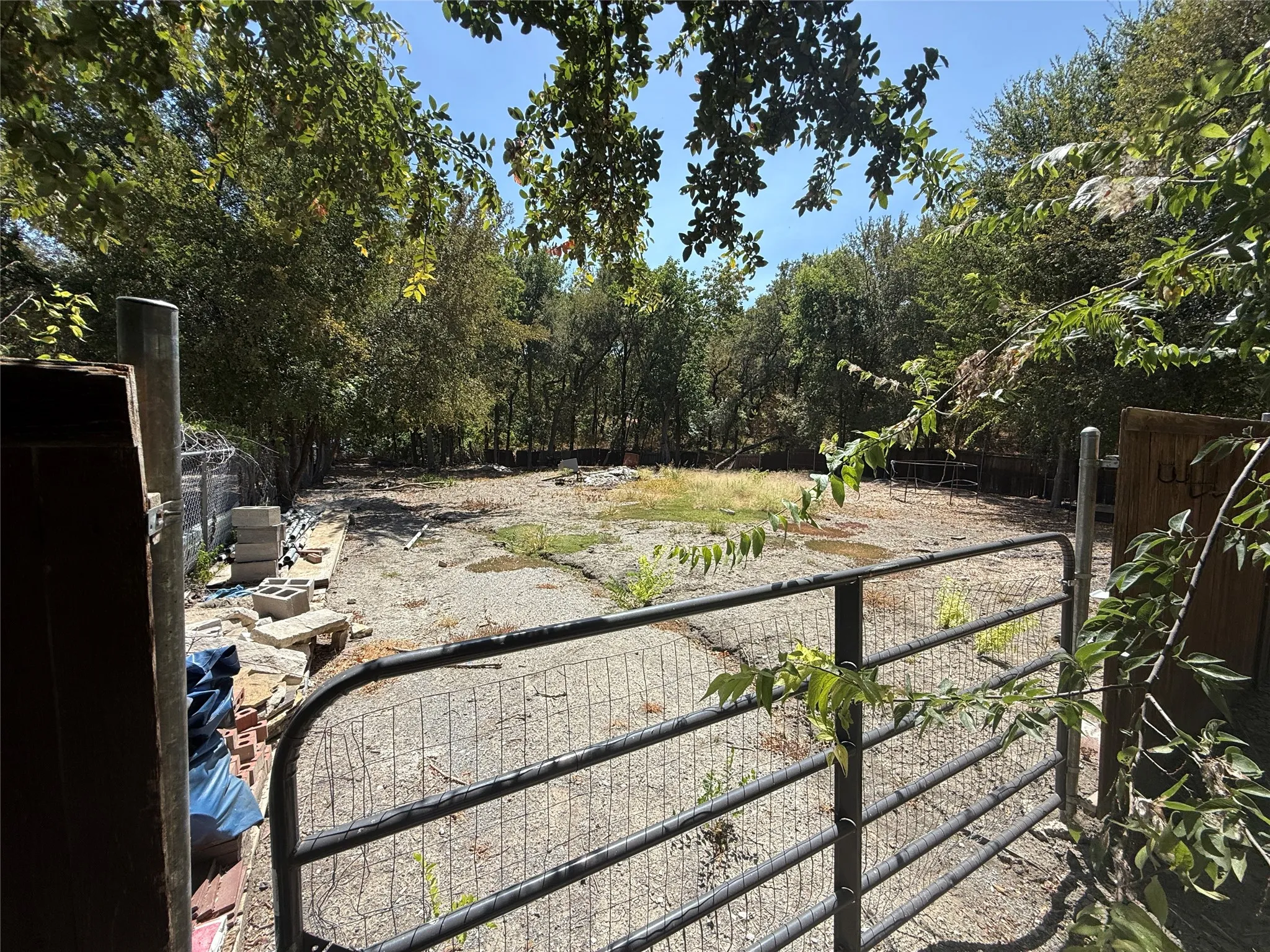 Expansive lot featuring a metal gate, established trees, and clear sky