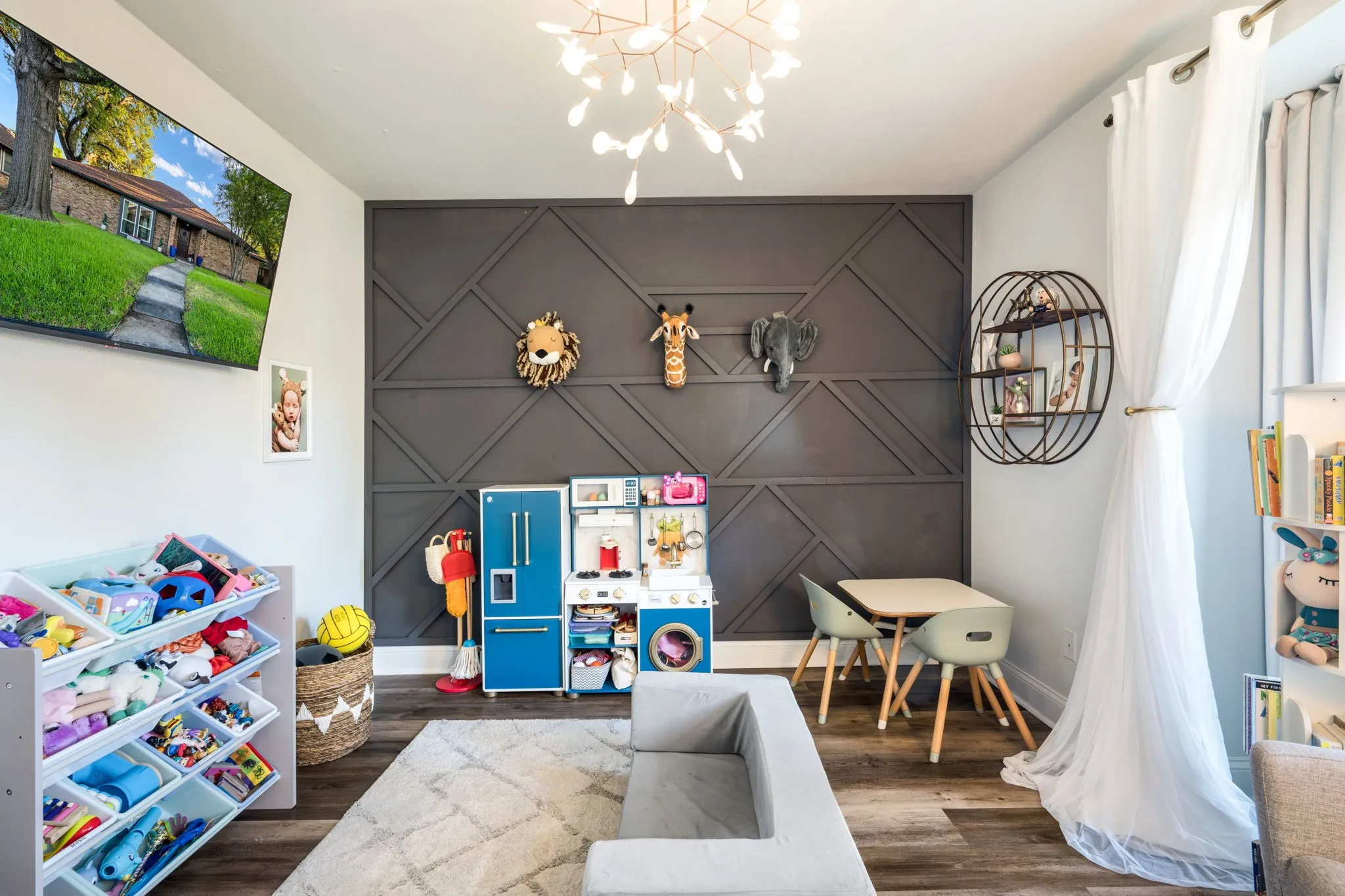 Geometric accent wall, modern chandelier, wood-finish flooring, white window sheers