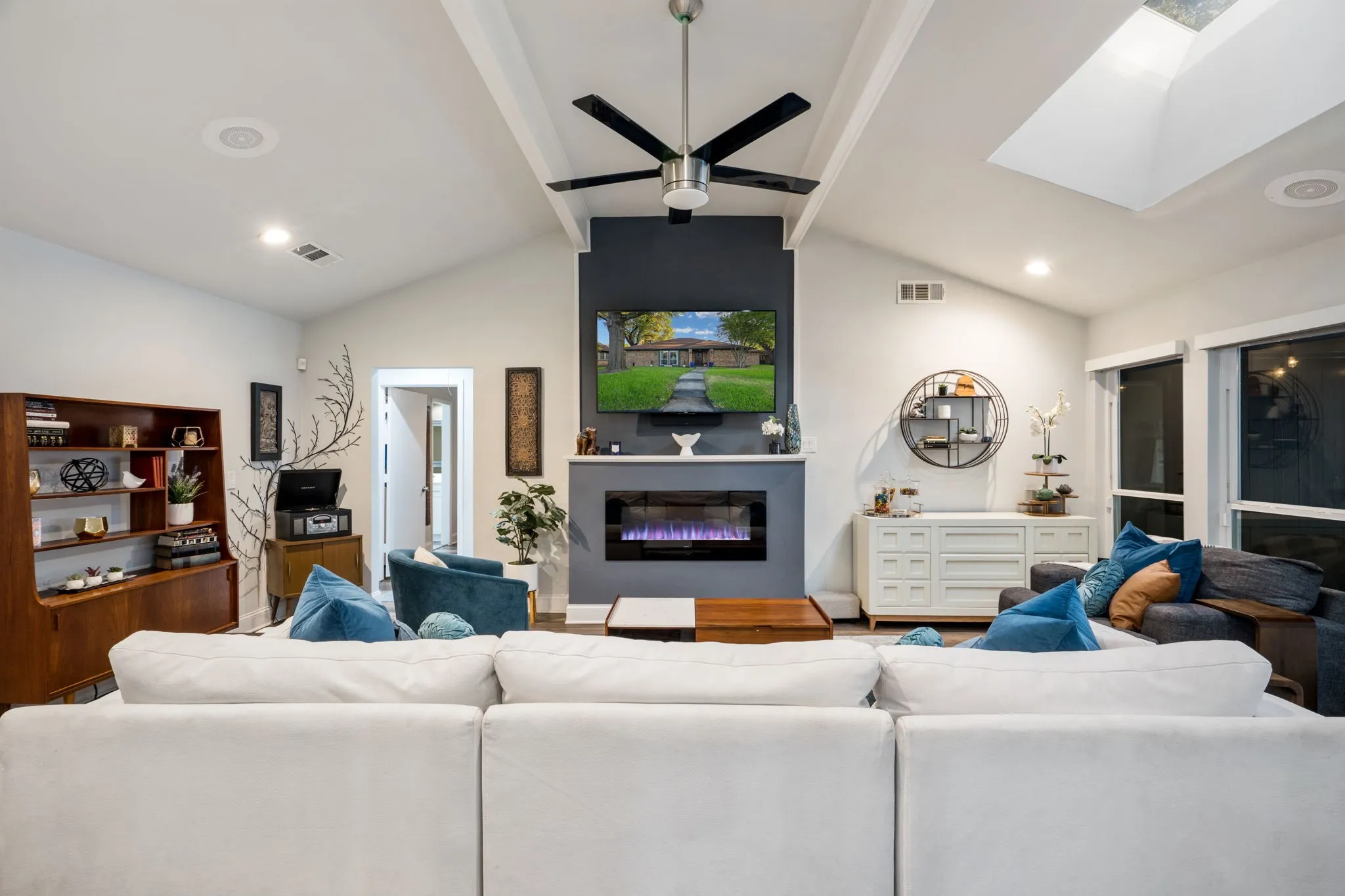 Vaulted ceilings with exposed beams, built-in recessed lighting, integrated electric fireplace, skylight, and large windows