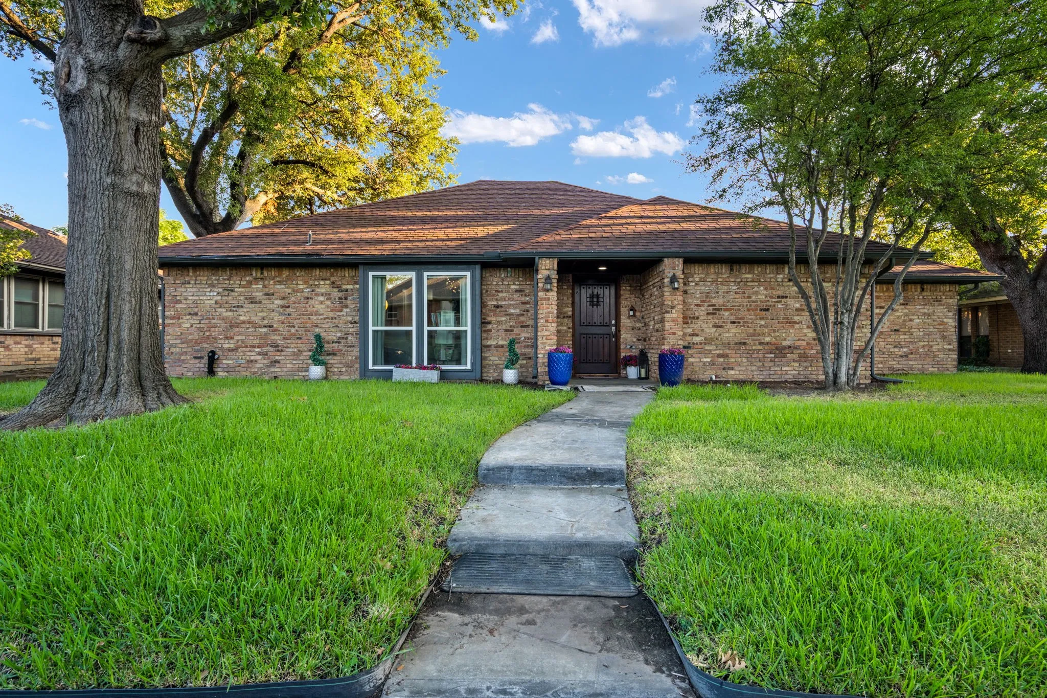 Brick exterior, dark brown roof, front entry with transom window, curved concrete pathway, mature trees