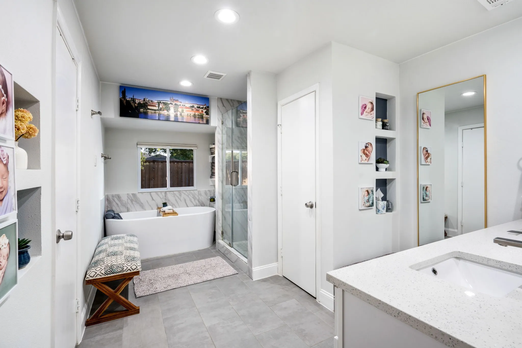 Freestanding soaking tub, glass-enclosed shower, built-in recessed shelving, integrated vanity with dual undermount sinks, and recessed ceiling lighting