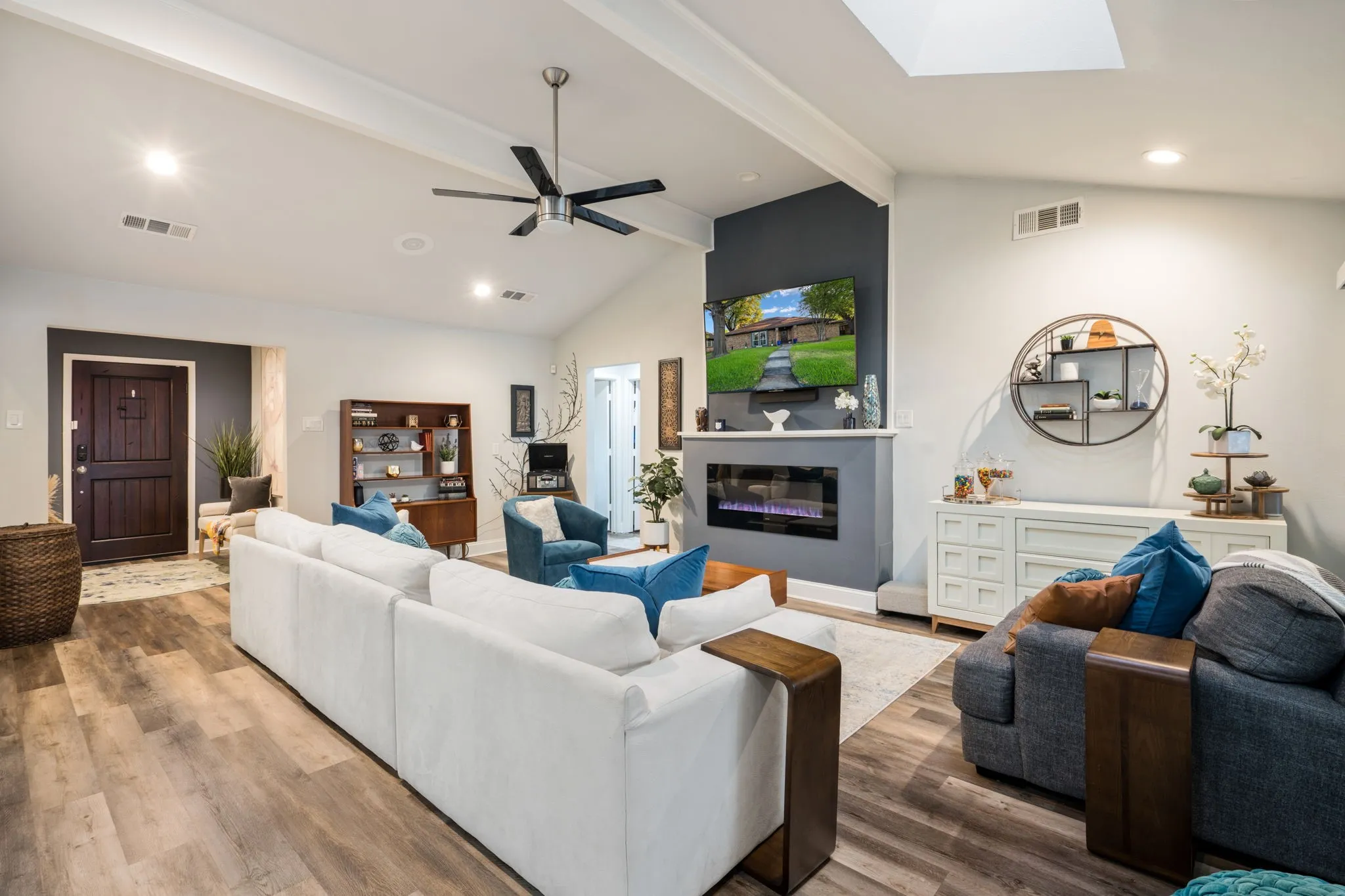 Vaulted ceiling with exposed beams, wood-finish flooring, built-in electric fireplace, and a skylight
