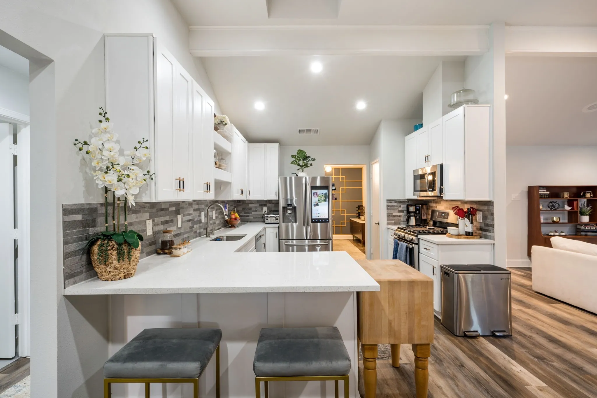 Kitchen featuring white cabinetry, stainless steel appliances, a multi-tone tile backsplash, light-toned countertops, and wood-finish flooring