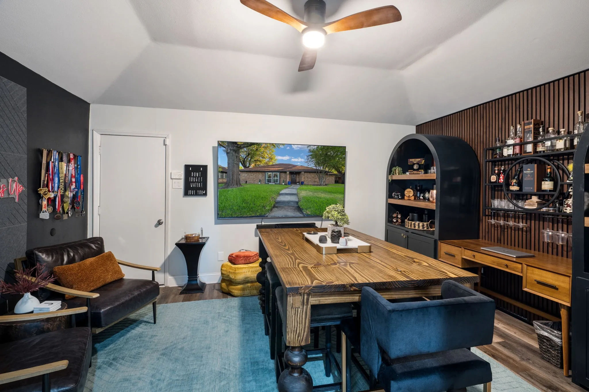 Bedroom currently being used as a game room,
vaulted ceiling with wood-finish ceiling fan, wood-finish flooring, built-in arched shelving units with wood backing, and a wood-slat accent wall