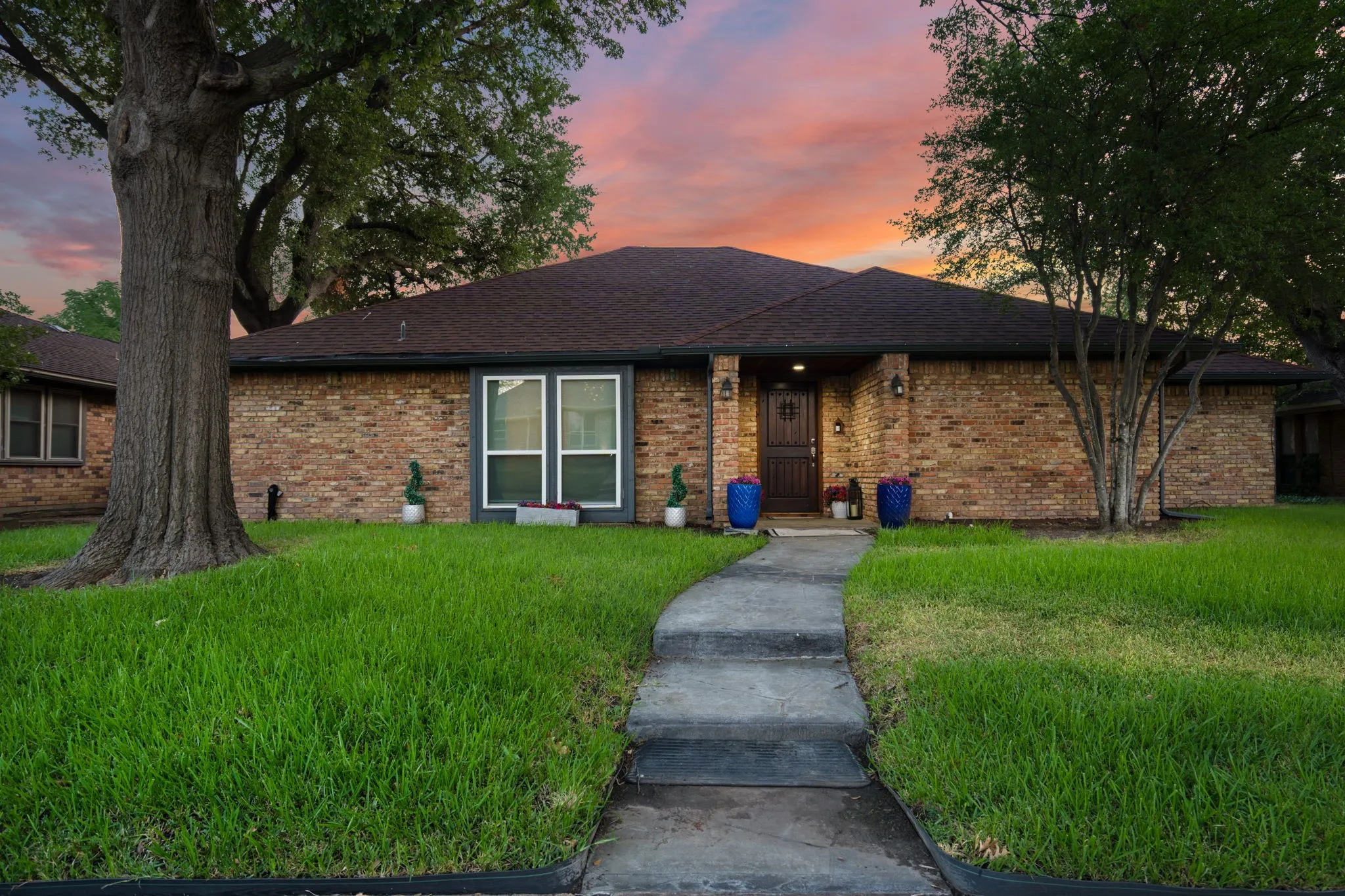 ranch style brick home with large trees and stamped concrete sidewalk