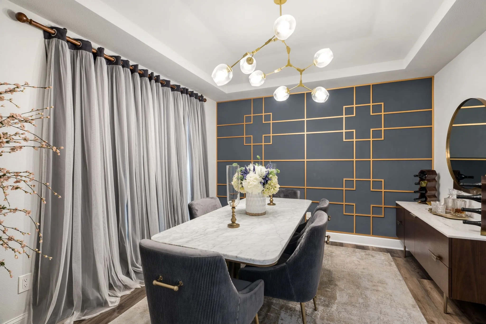 Tray ceiling with a modern chandelier, accent wall with geometric molding, and wood-finish flooring