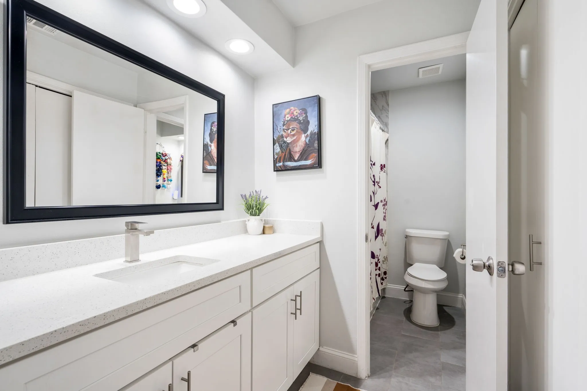 Recessed lighting illuminates the vanity with an integrated sink and brushed nickel faucet, set within white cabinetry and a light stone countertop
