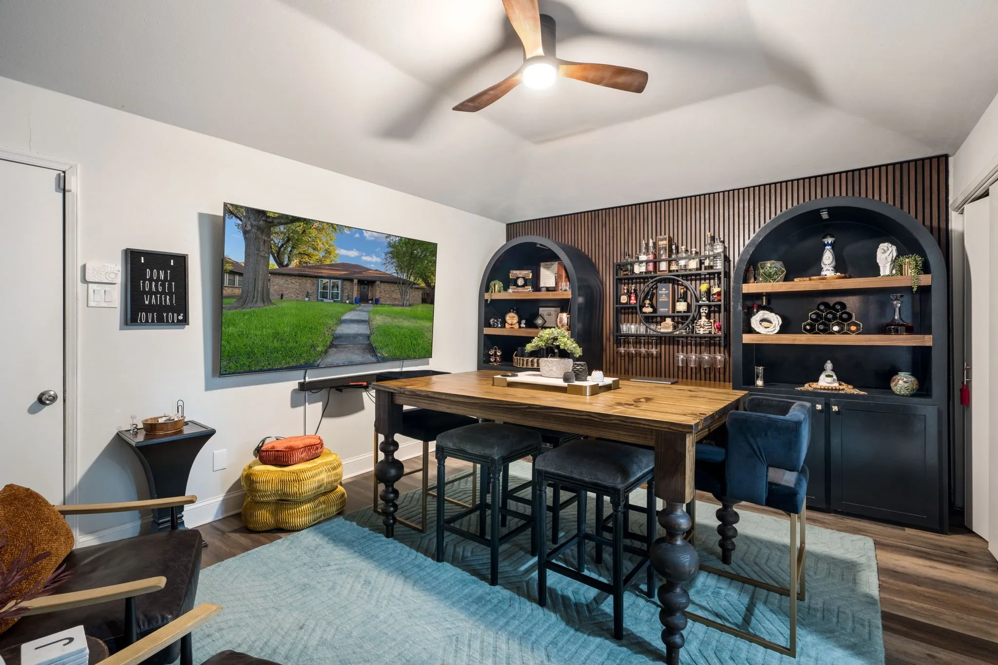Bedroom currently being used as a game room,
vaulted ceiling with wood-finish ceiling fan, wood-finish flooring, built-in arched shelving units with wood backing, and a wood-slat accent wall