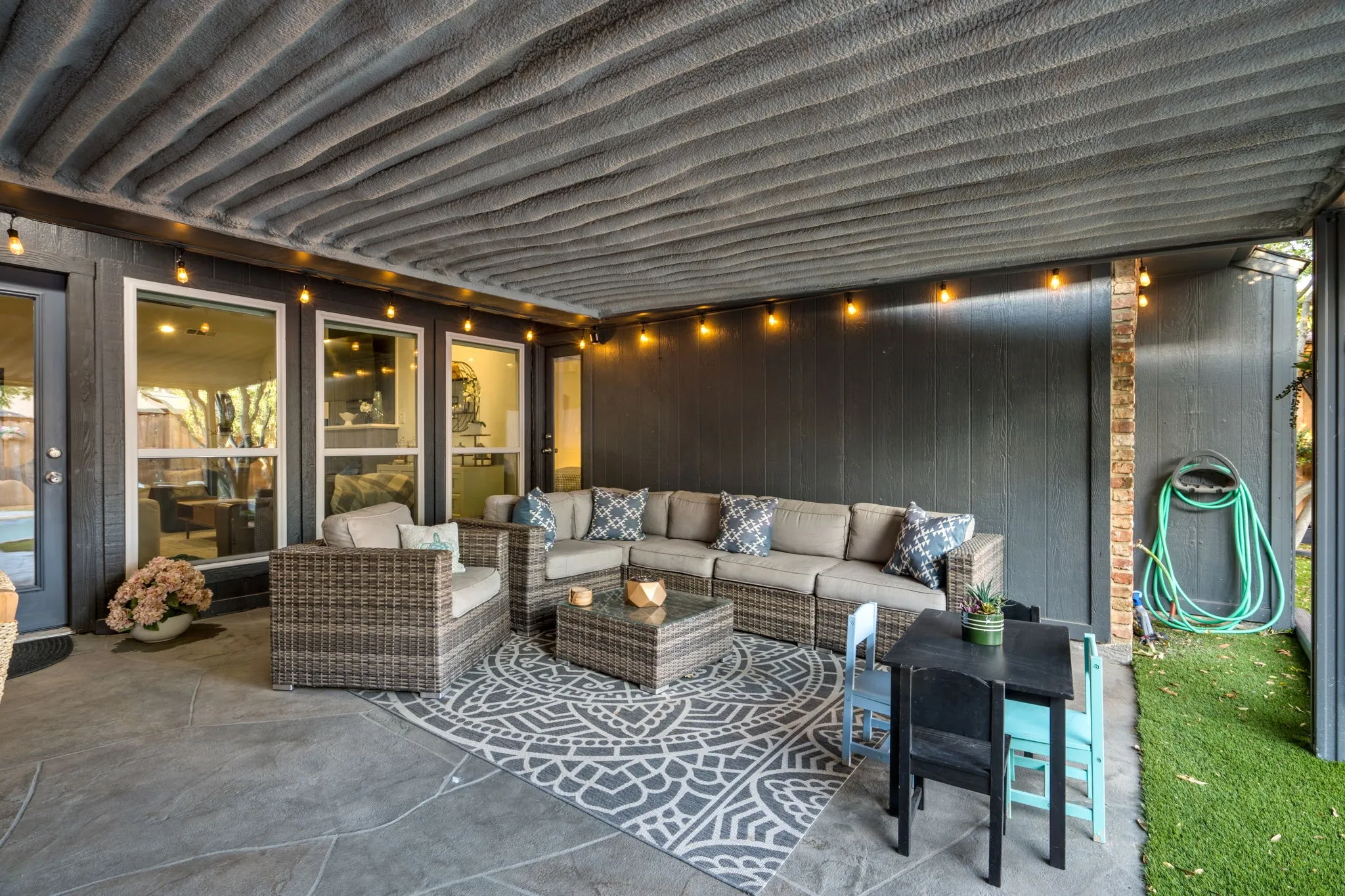 Covered patio with stamped concrete flooring, multiple windows, brick column, and artificial turf.  Insulated cover keeps area cooler during the summer months