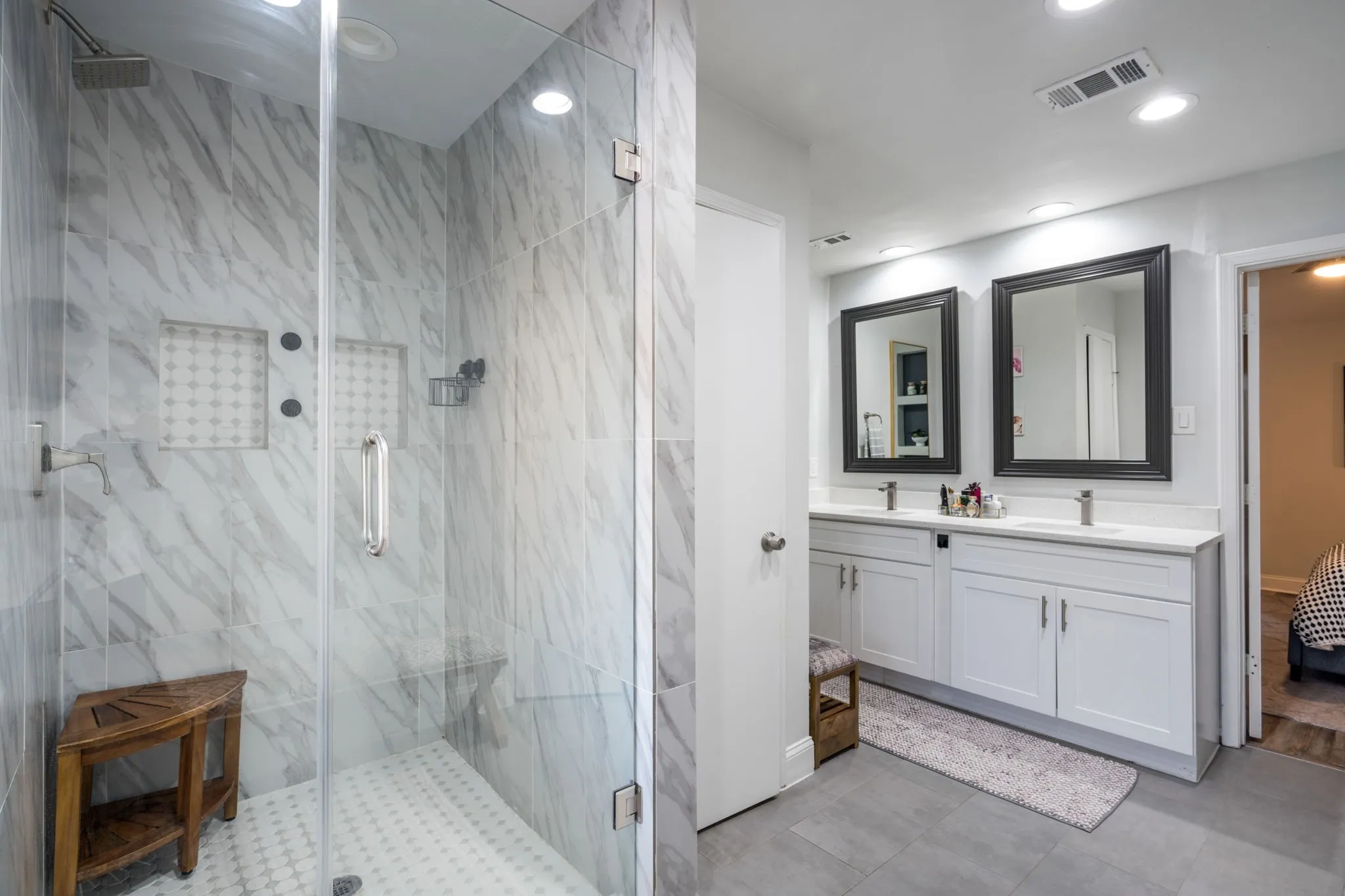 Walk-in shower with full-height tile surround and dual recessed niches, dual sink vanity with stone countertops, WC