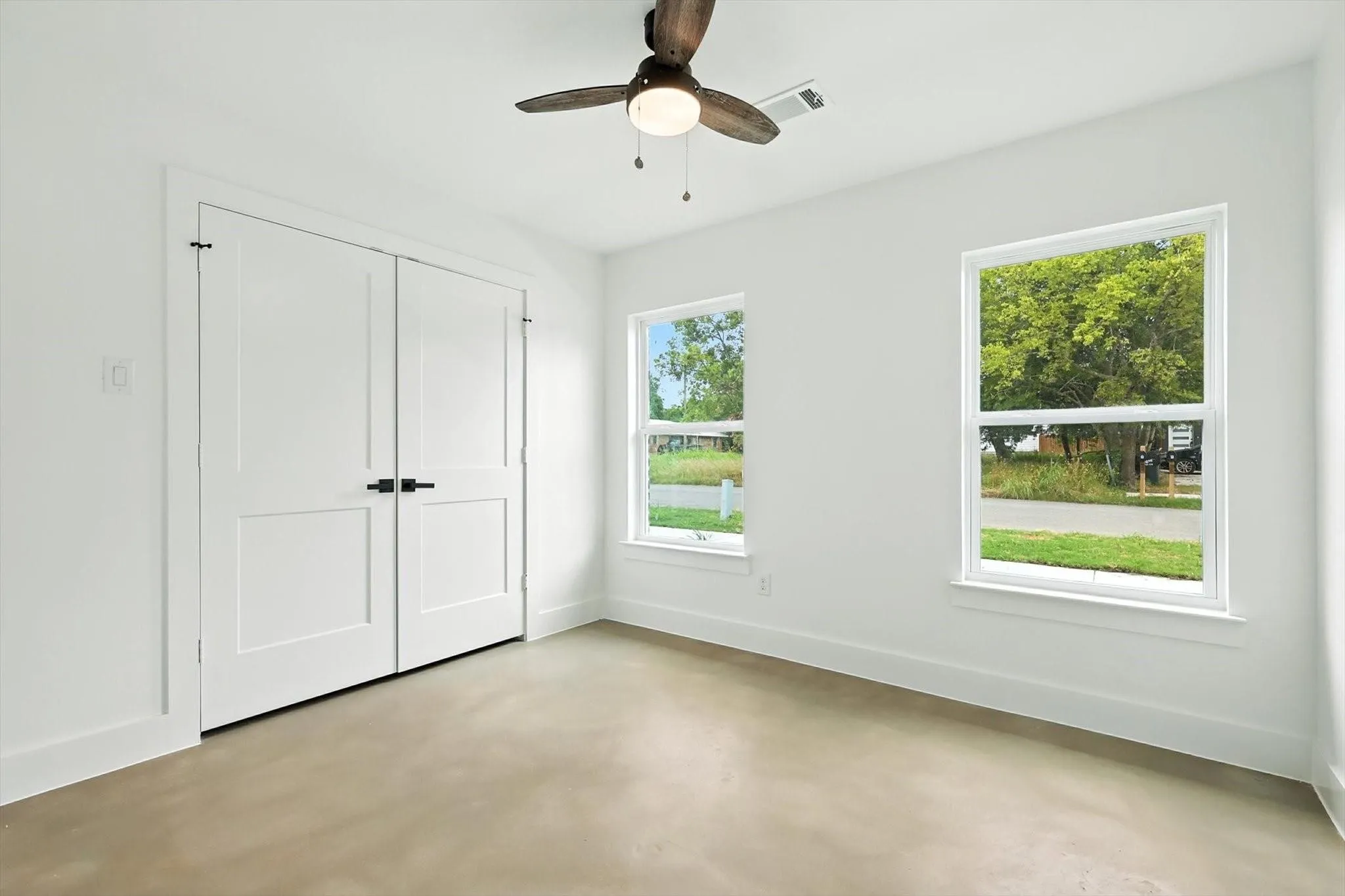 Light-filled room featuring a ceiling fan, two windows, two-panel bifold doors with matte black hardware, and light-colored flooring