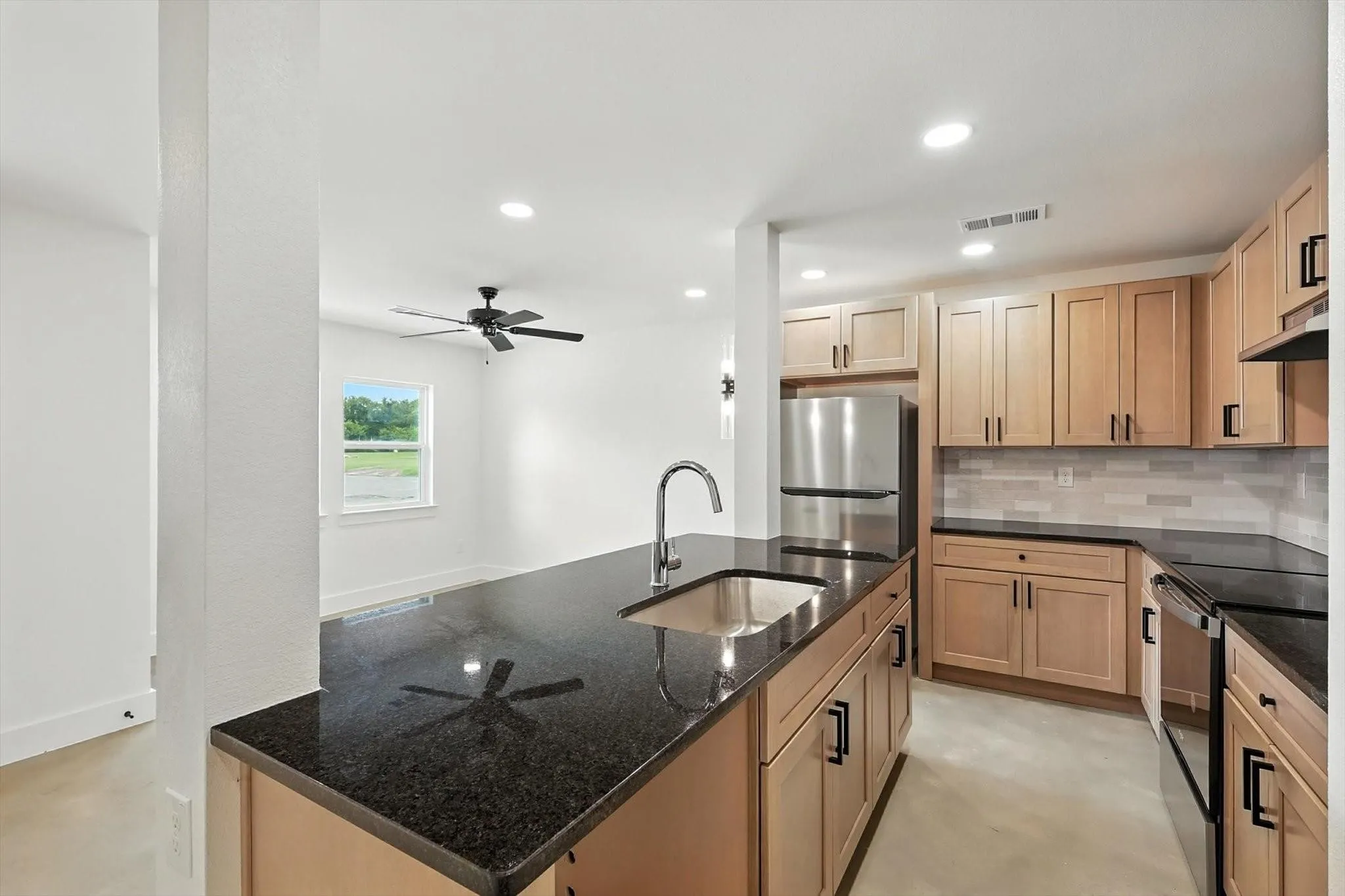 Kitchen featuring dark granite countertops, light wood-finish cabinetry, stainless steel appliances, and a tile backsplash