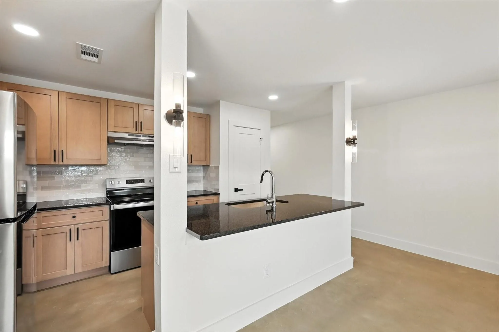 Kitchen featuring wood-finish cabinetry, stainless steel appliances, dark countertops, and a tiled backsplash