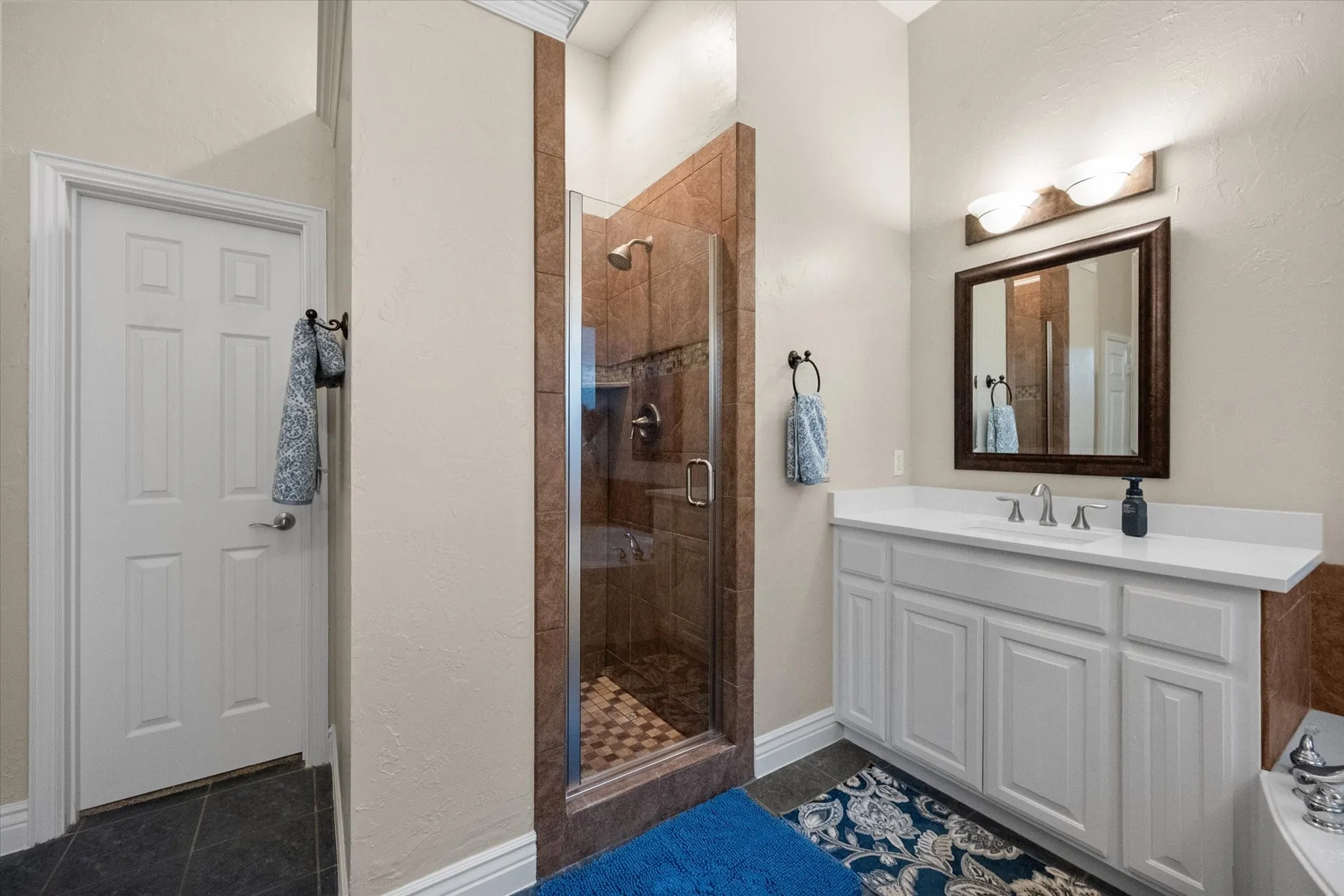 Glass-enclosed shower with tile surround, single vanity with white cabinetry, solid surface countertop, and framed mirror
