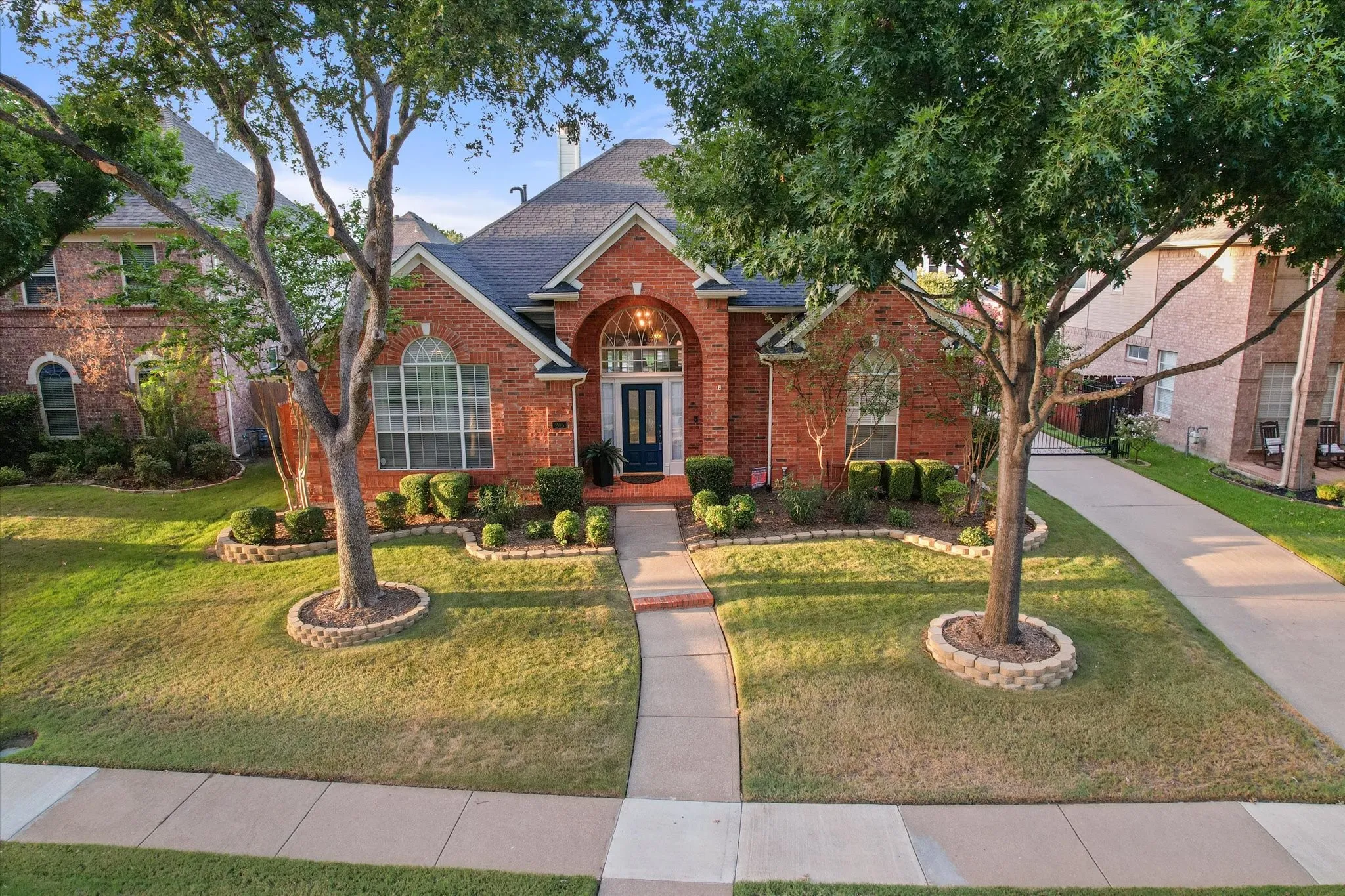 Brick exterior with arched entry, gabled roofline, mature trees, and a paved driveway