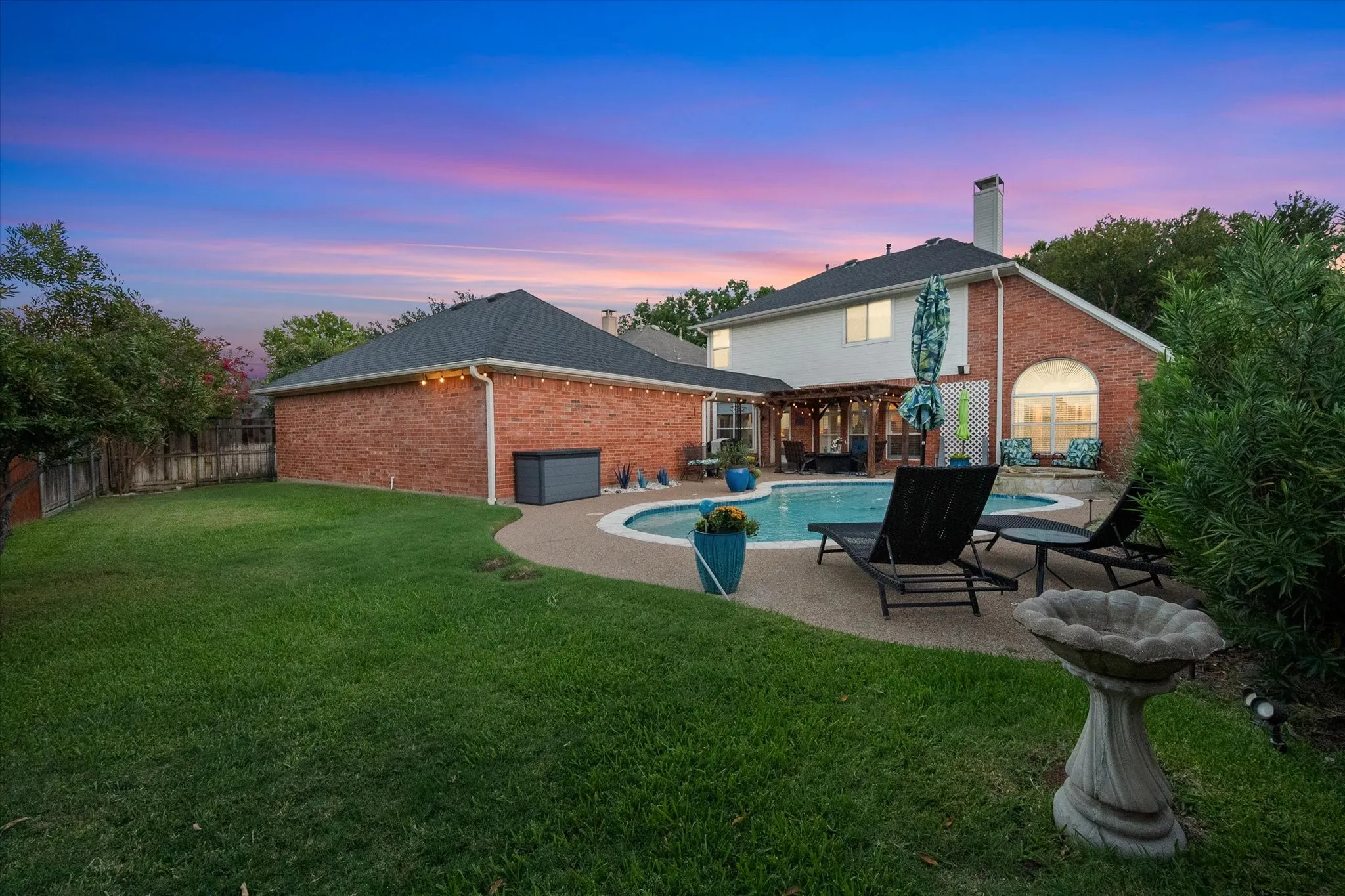 Expansive backyard featuring a manicured lawn, a swimming pool with a surrounding hardscaping, and a brick exterior on the main residence