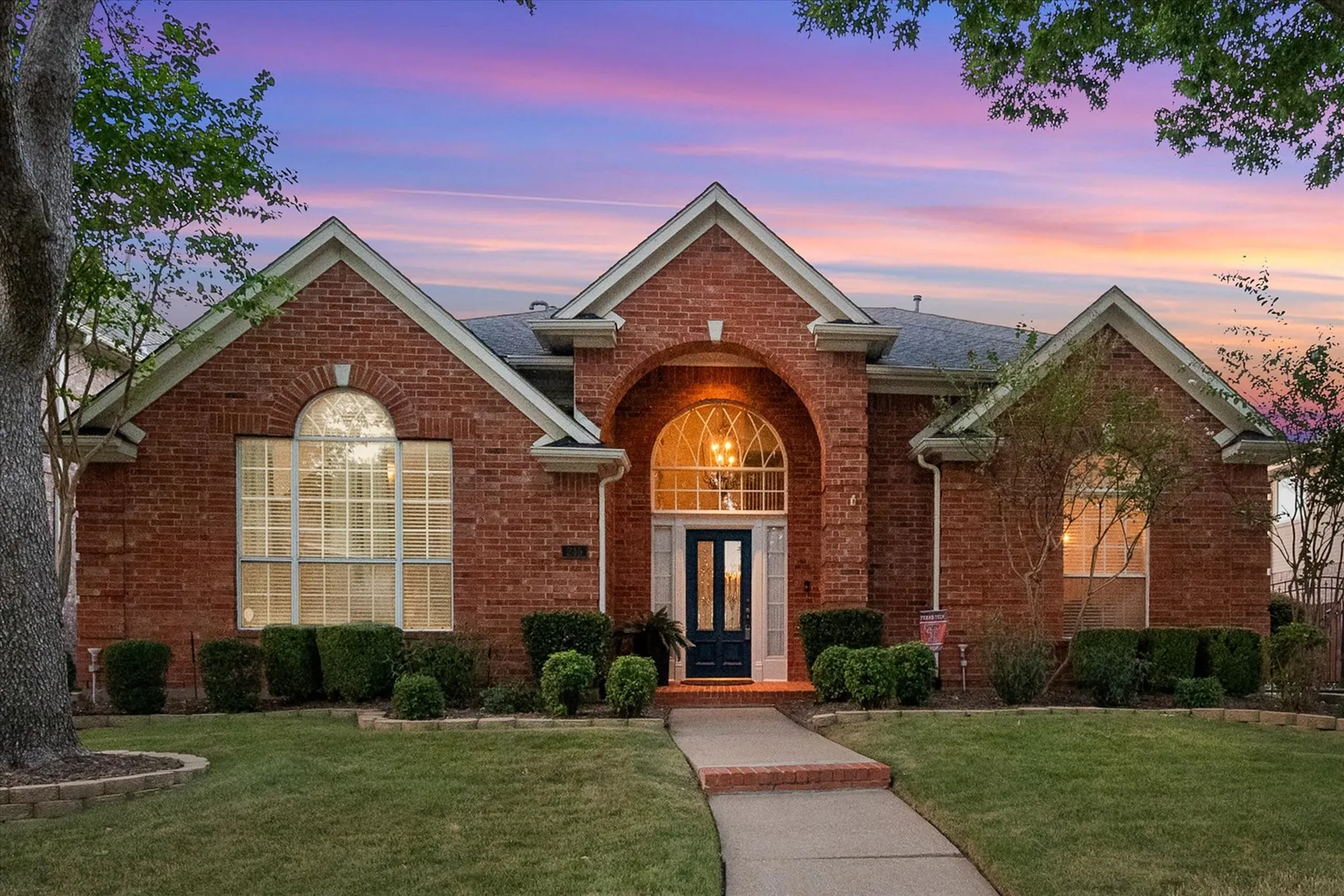 Brick exterior with multiple gables, arched entry, formal entry door, and established landscaping