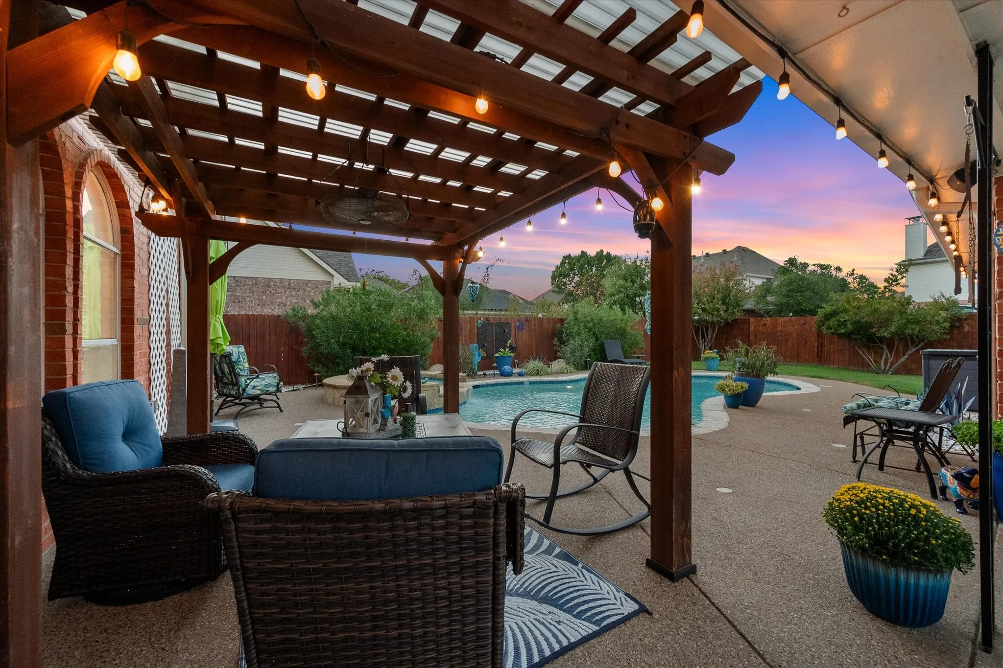 Expansive outdoor living area featuring a built-in swimming pool, a wood pergola with integrated lighting, and a brick exterior wall with an arched window
