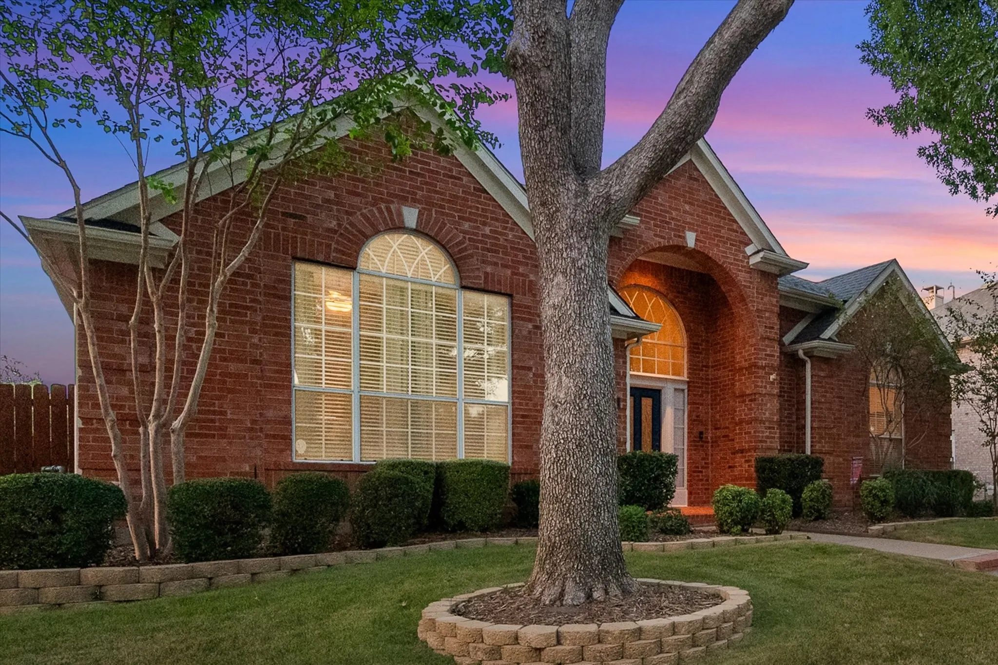 Brick exterior with arched windows, prominent entryway, mature trees, and landscaped shrubbery