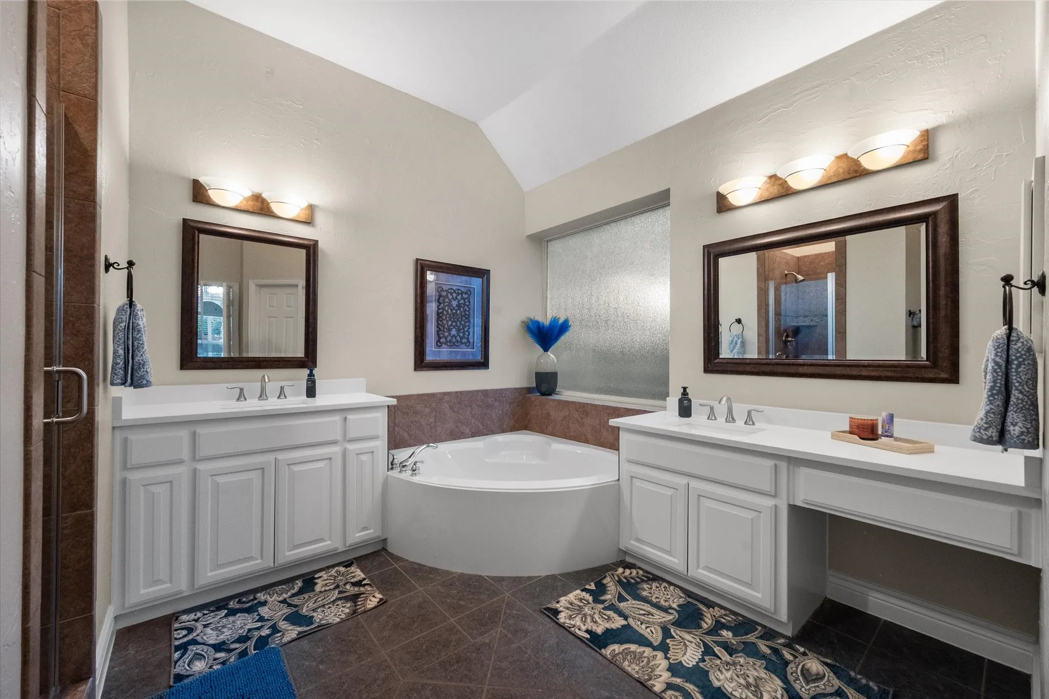 Dual vanities with white cabinetry and integrated sinks, corner soaking tub, and a separate shower enclosure
