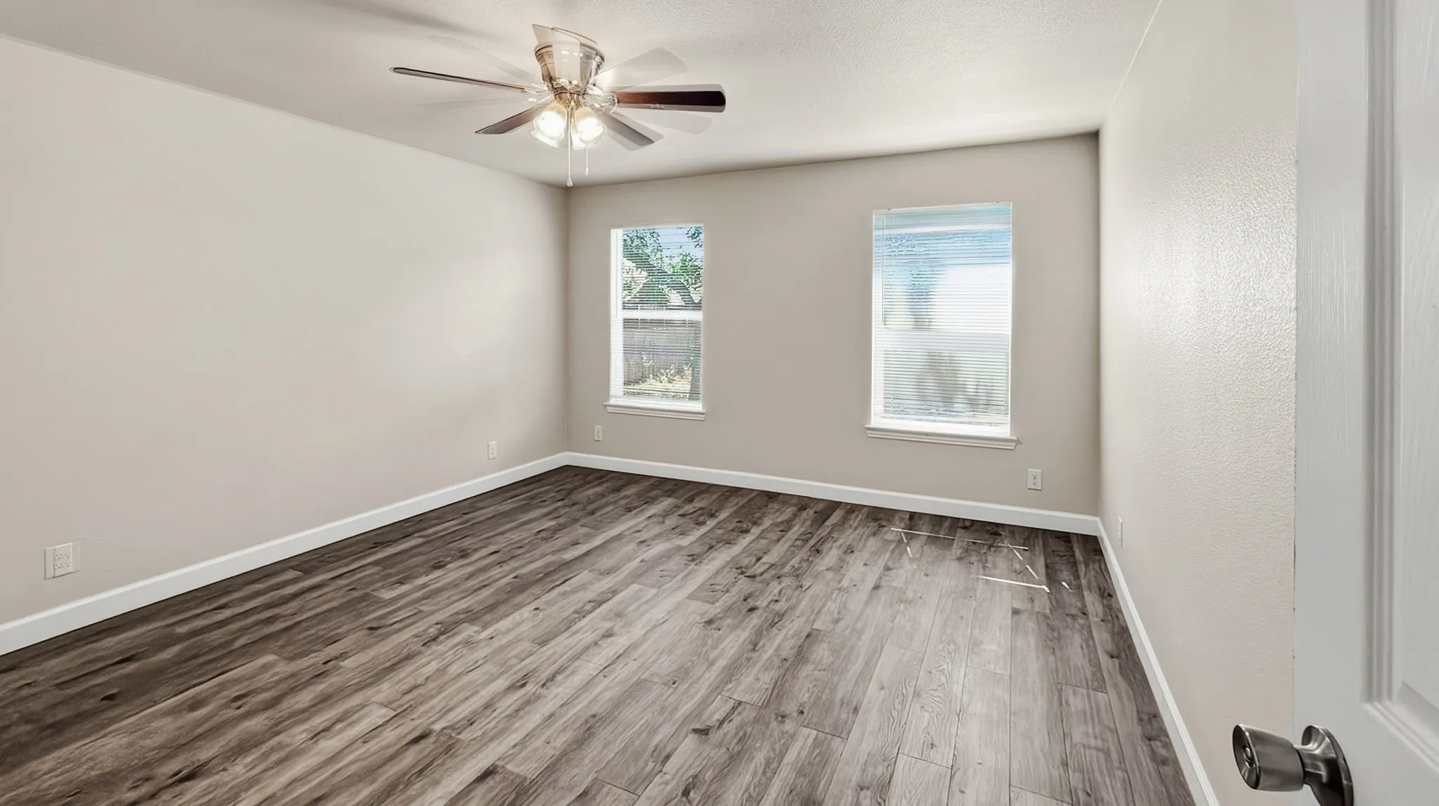 Spacious room featuring wood-finish flooring, two windows, and a ceiling fan with integrated lighting