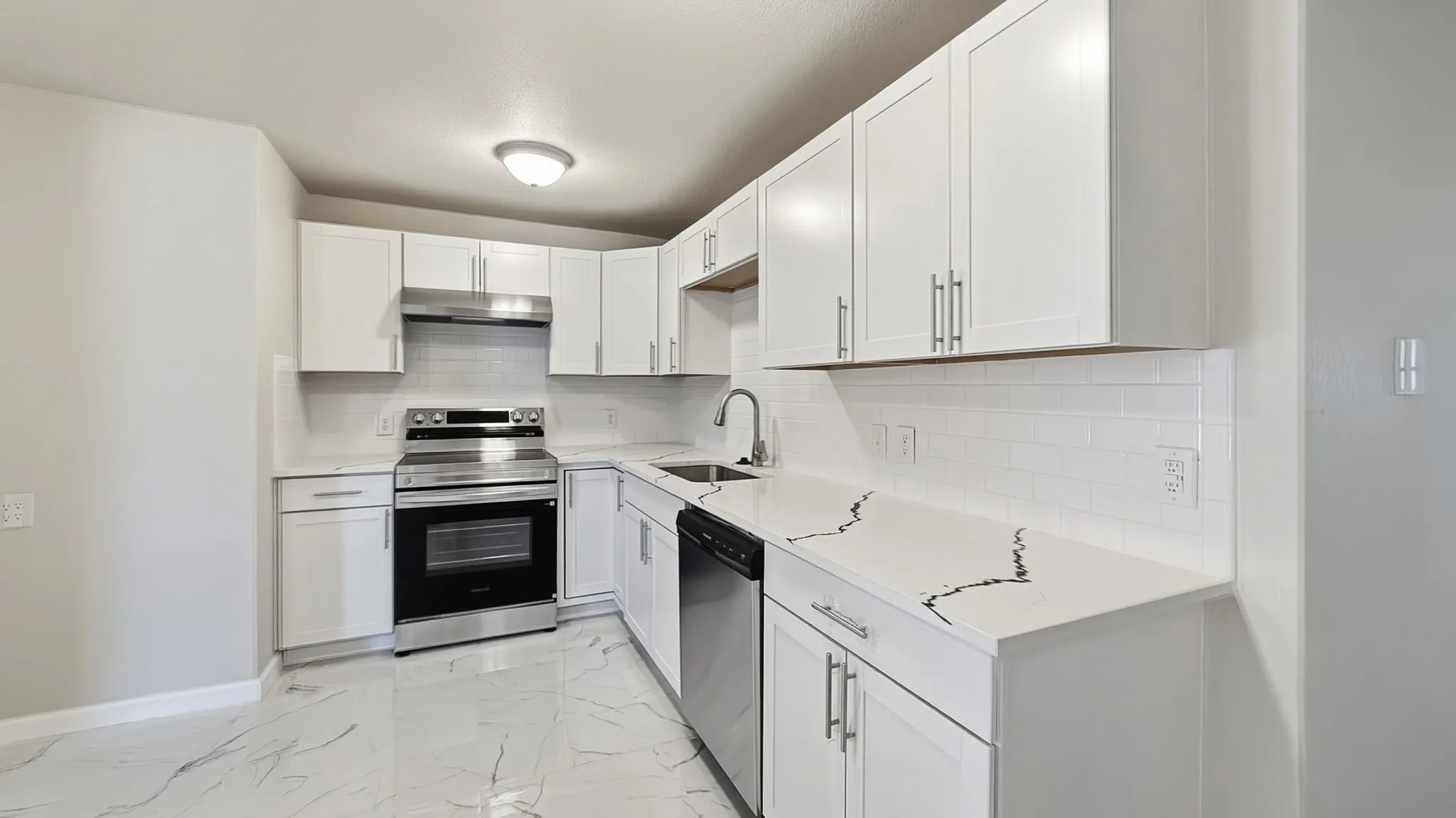 Kitchen featuring white shaker-style cabinetry, stainless steel appliances, white subway tile backsplash, and light-colored countertops with dark veining