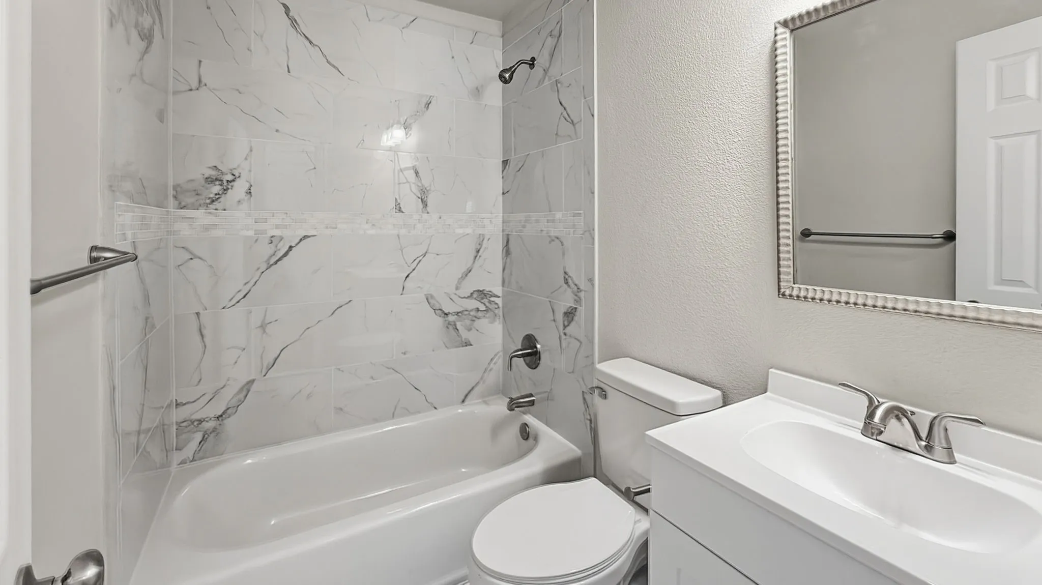 Bathroom featuring a white bathtub, marble-look tiled shower surround with decorative accent tile, white vanity with integrated sink, and a framed mirror