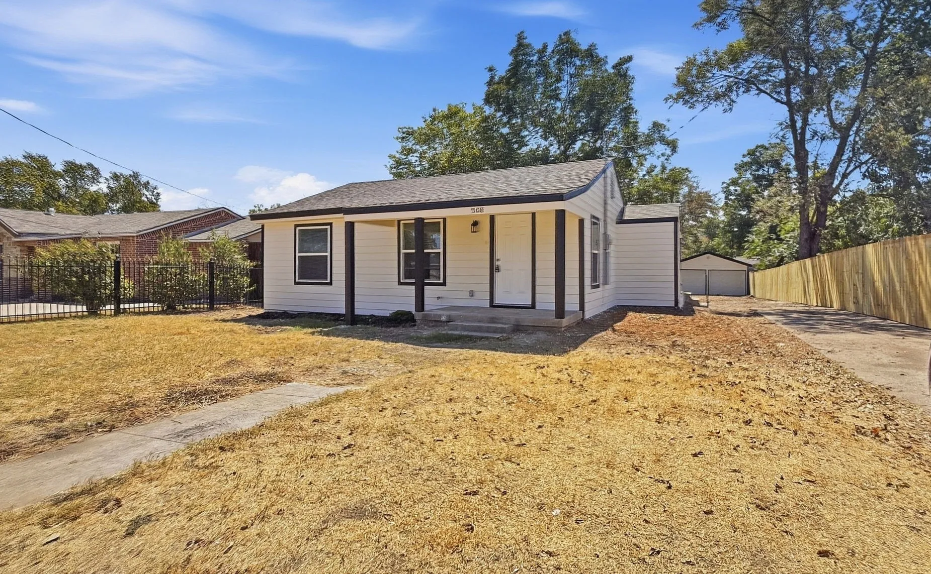 White exterior with dark trim, covered front porch, concrete walkway, detached garage structure, and privacy fencing