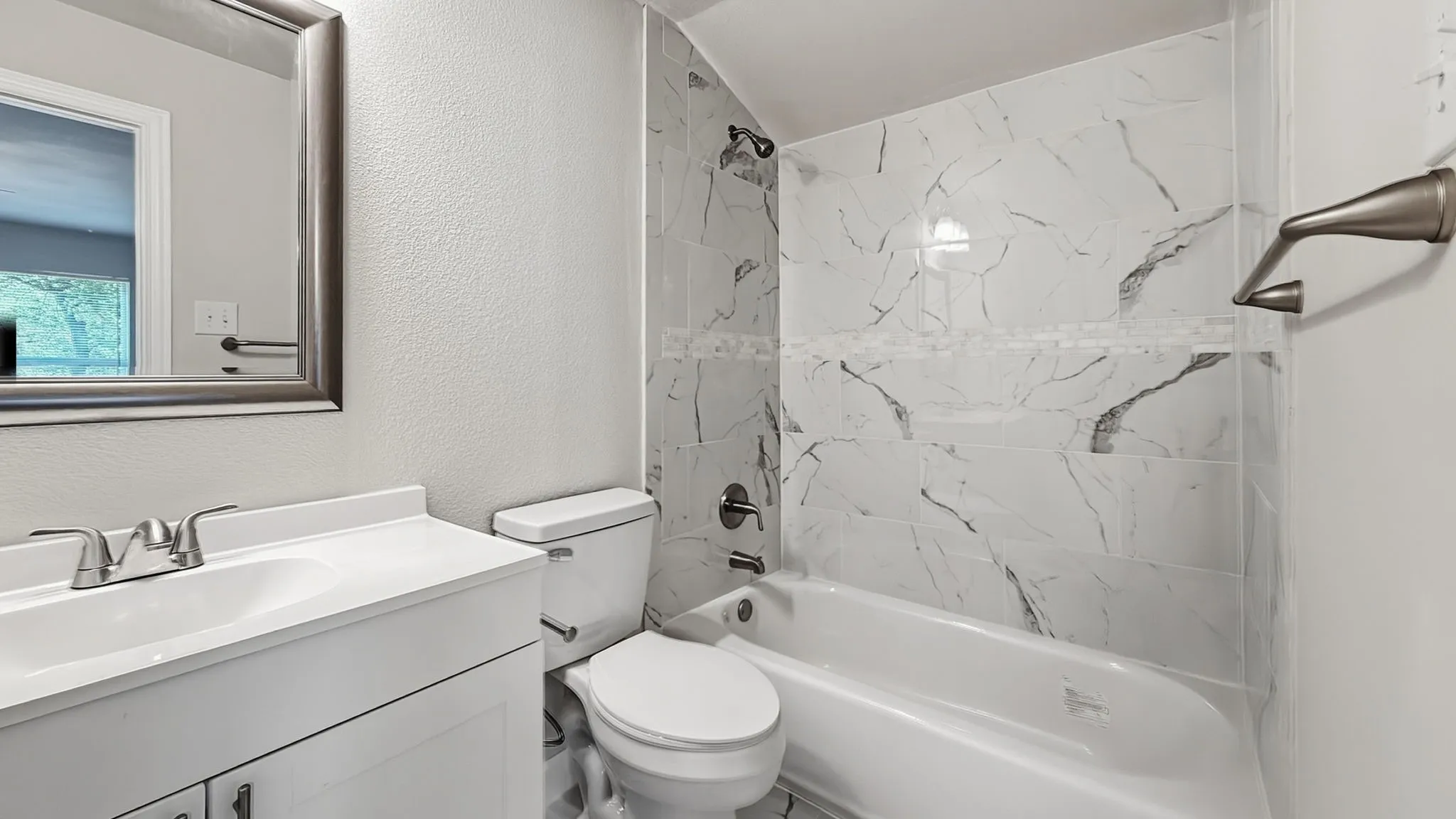 Bathroom featuring a white vanity with integrated sink, chrome faucet, toilet, and a bathtub with a tiled surround