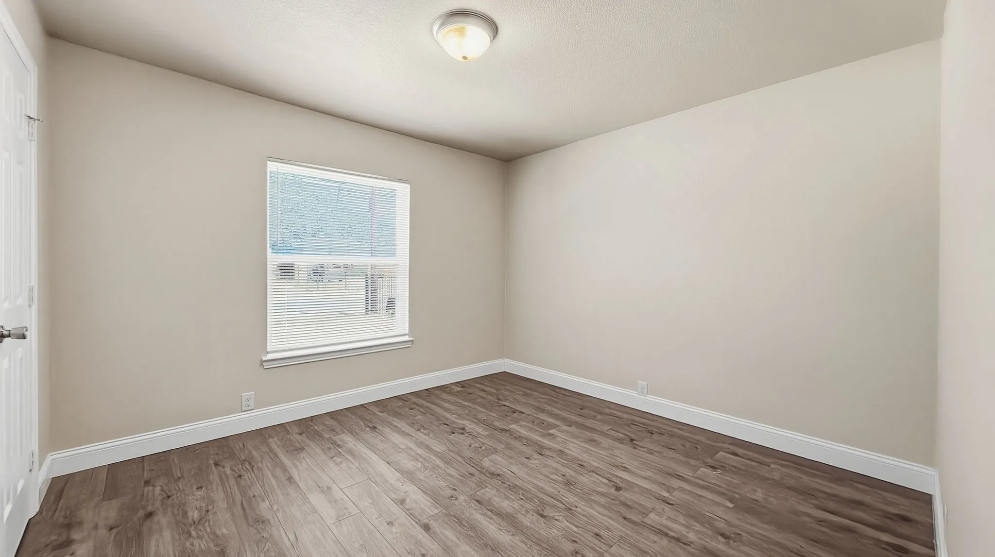 Wood-finish flooring with white trim, neutral wall paint, and a single window with blinds