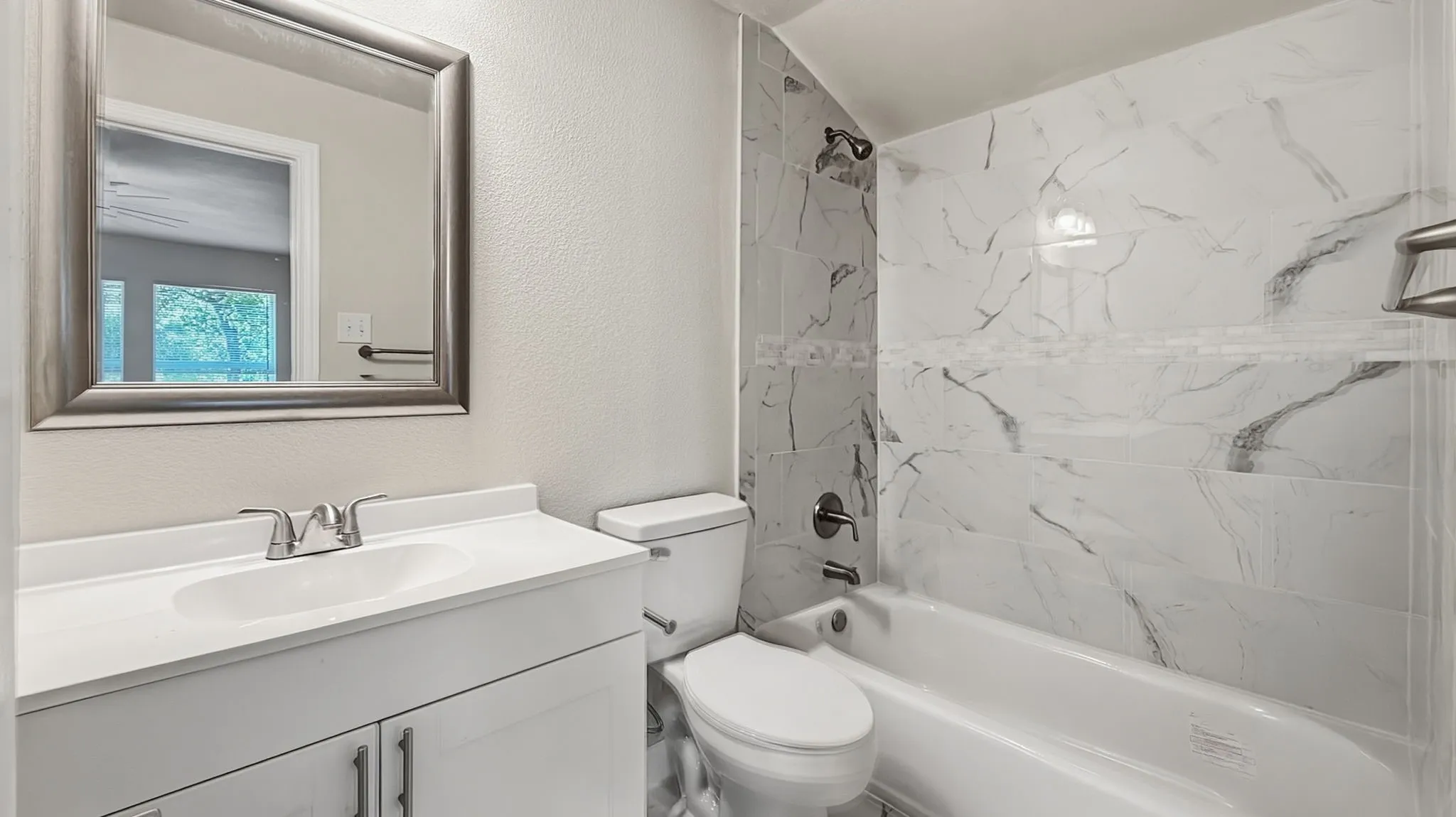 Bathroom featuring a white vanity with integrated sink, chrome faucet, framed mirror, white toilet, and a tiled shower with contrasting accent band