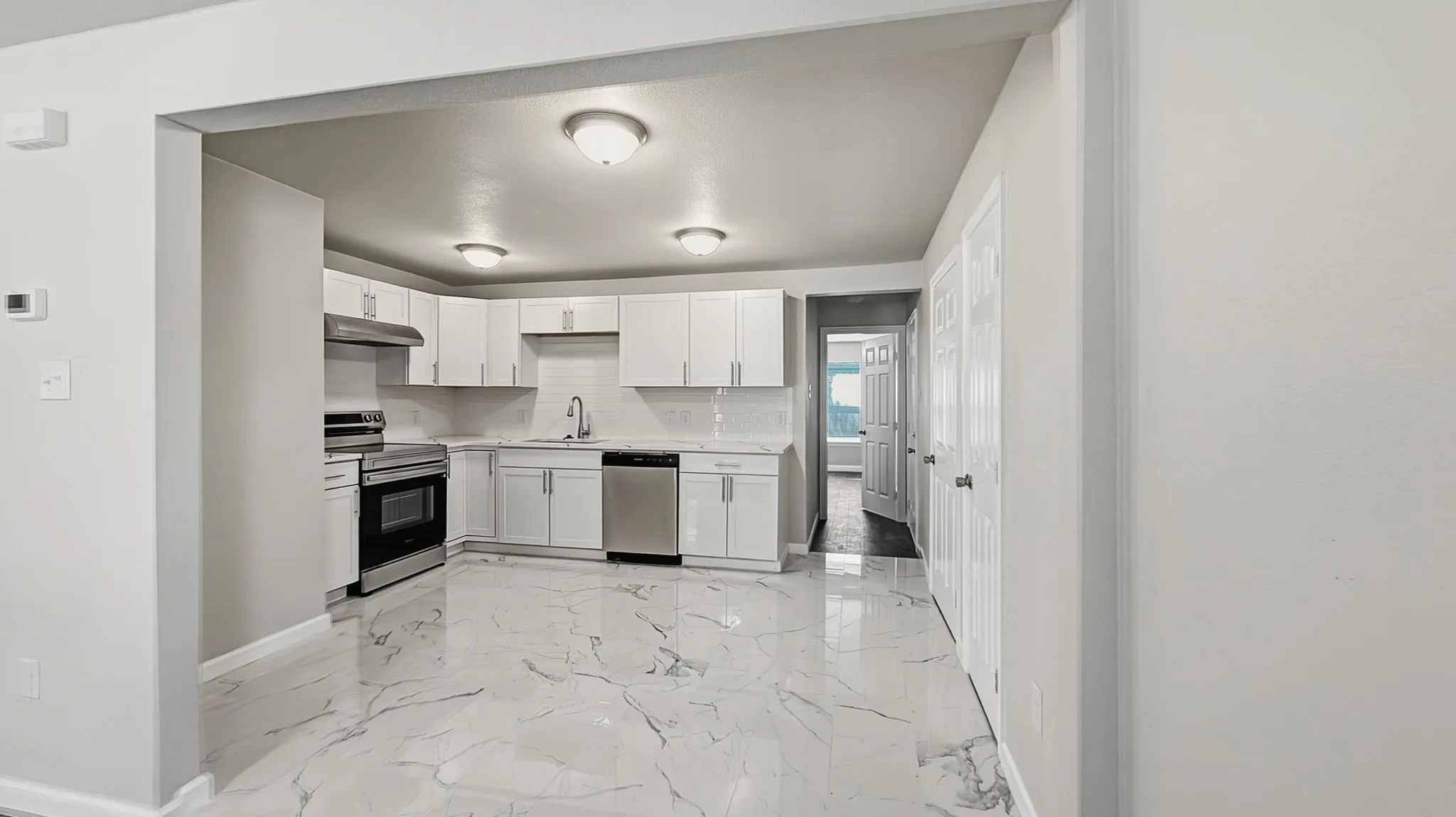 Kitchen featuring white shaker-style cabinetry, stainless steel appliances, white subway tile backsplash, and light-colored countertops with dark veining