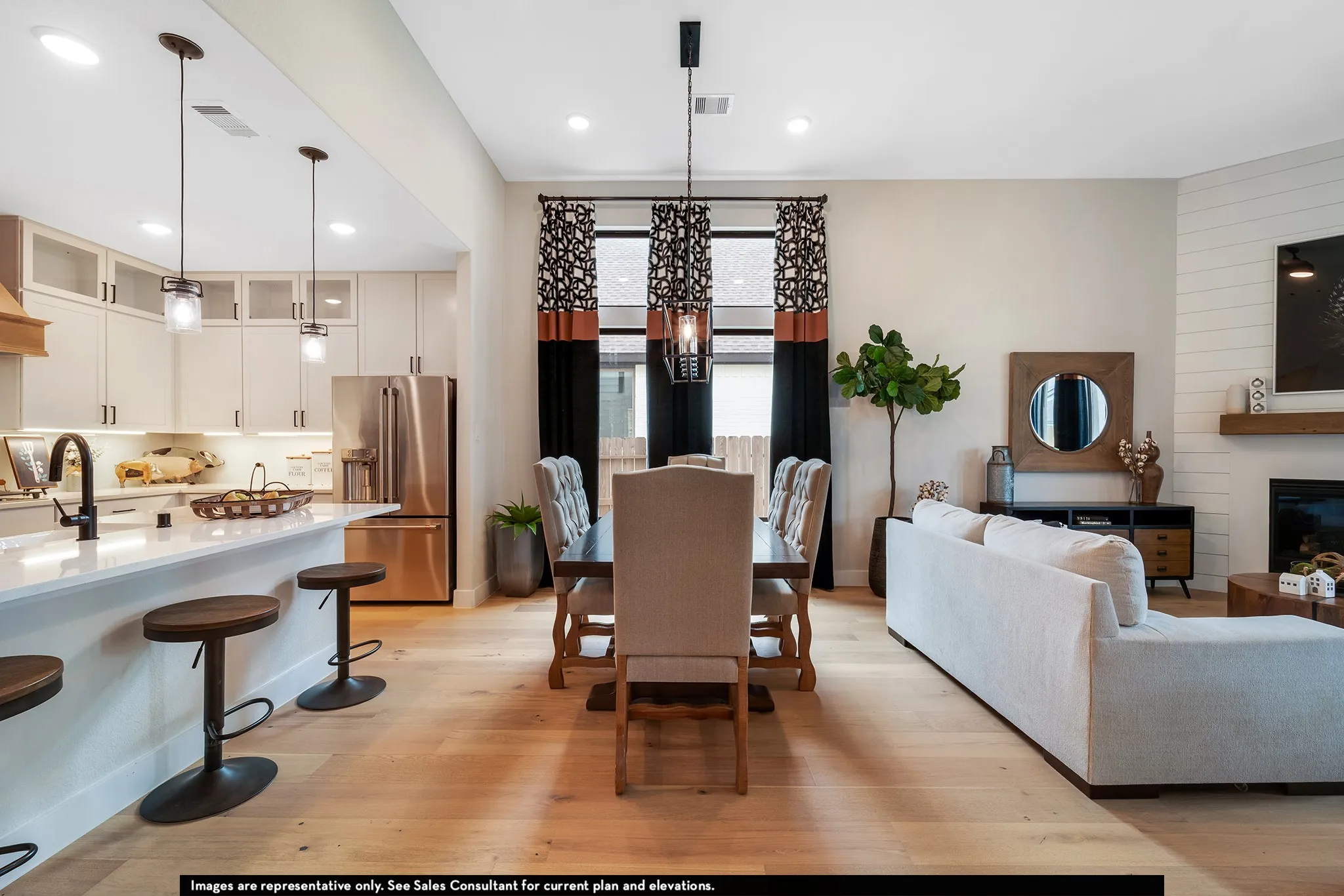 Open-concept living area featuring light wood-finish flooring, a kitchen island with pendant lighting, integrated stainless steel appliances, a shiplap accent wall, and a fireplace with a wood mantle