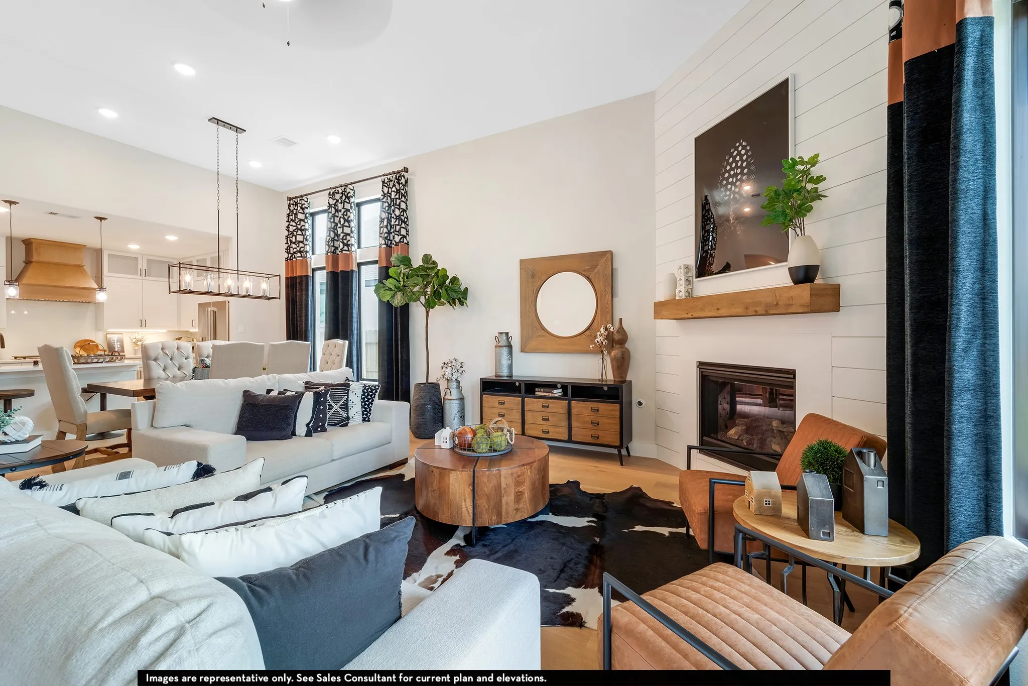 Open-concept living area featuring high ceilings, a linear electric fireplace with a wood mantel, wood-finish flooring, and a kitchen with white cabinetry and a wood range hood