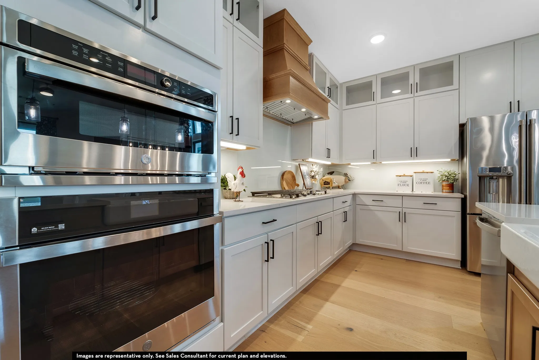 Built-in stainless steel double oven, white shaker-style cabinetry, wood-finish flooring, undermount sink, and stainless steel French door refrigerator