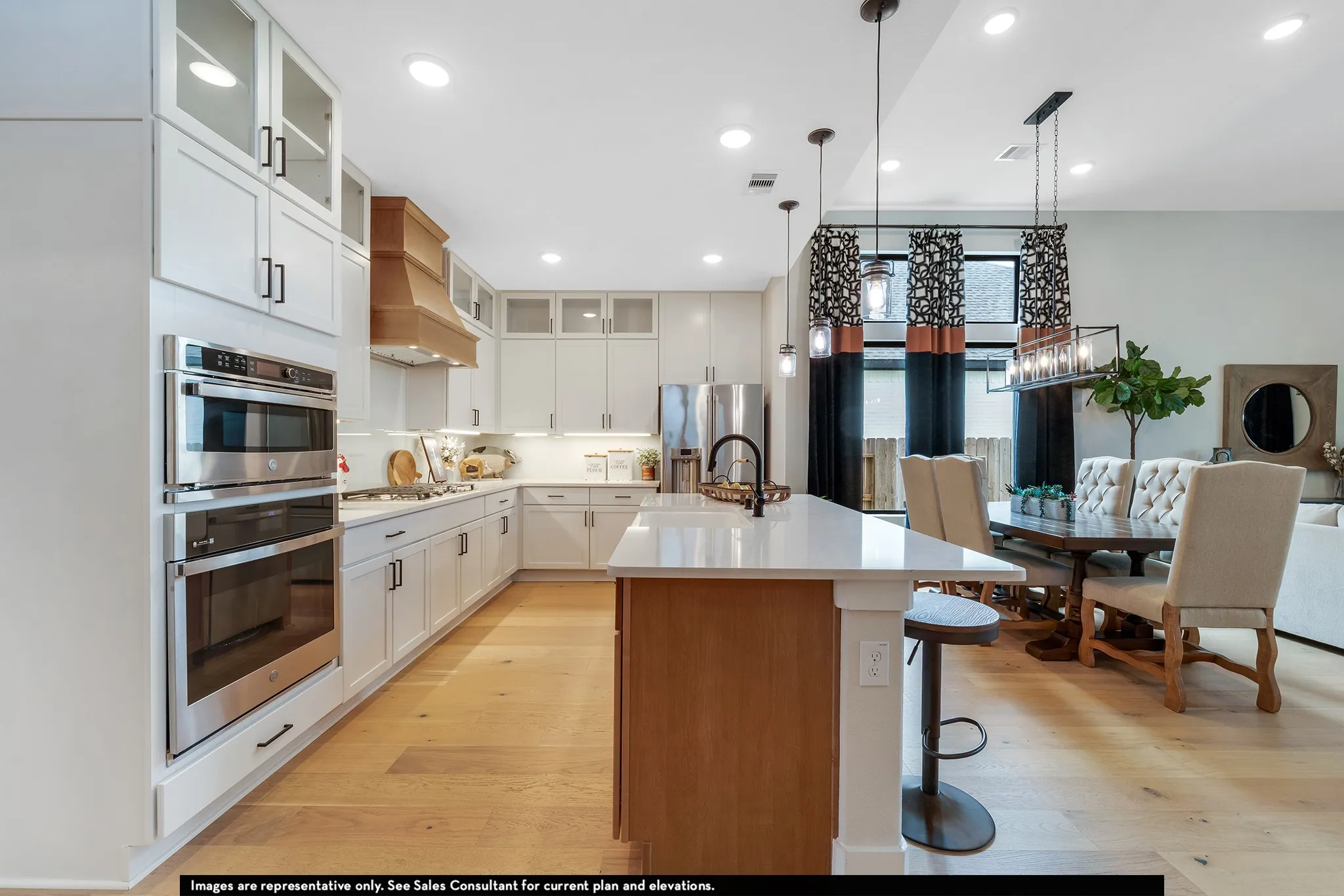 Gourmet kitchen with white cabinetry, stainless steel double ovens, and a natural wood range hood