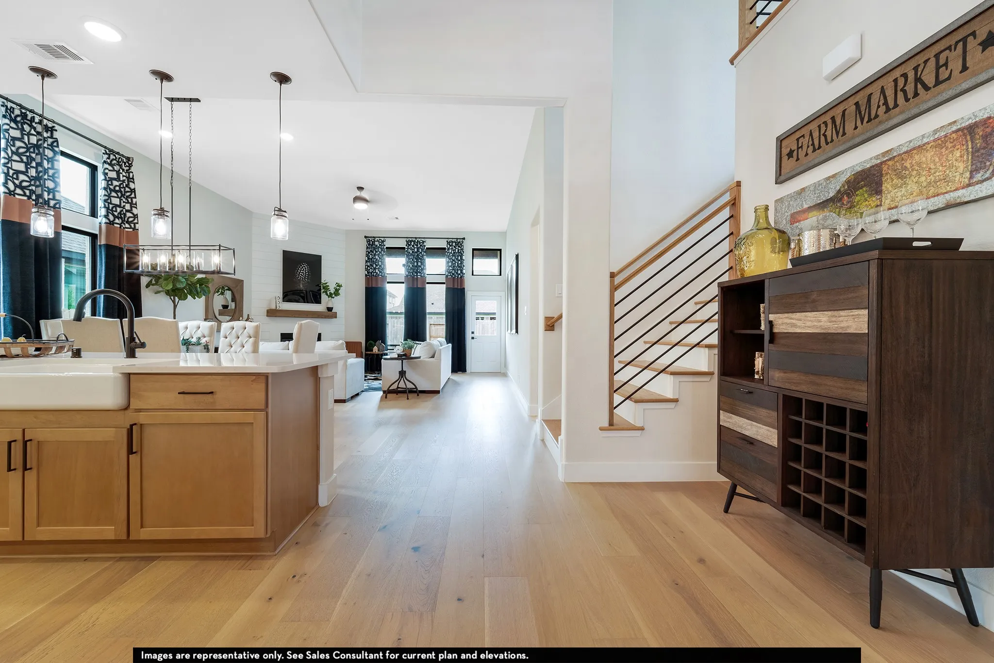 Open concept floor plan featuring light wood-finish flooring, a kitchen island with a farmhouse sink, and a staircase with a modern railing design