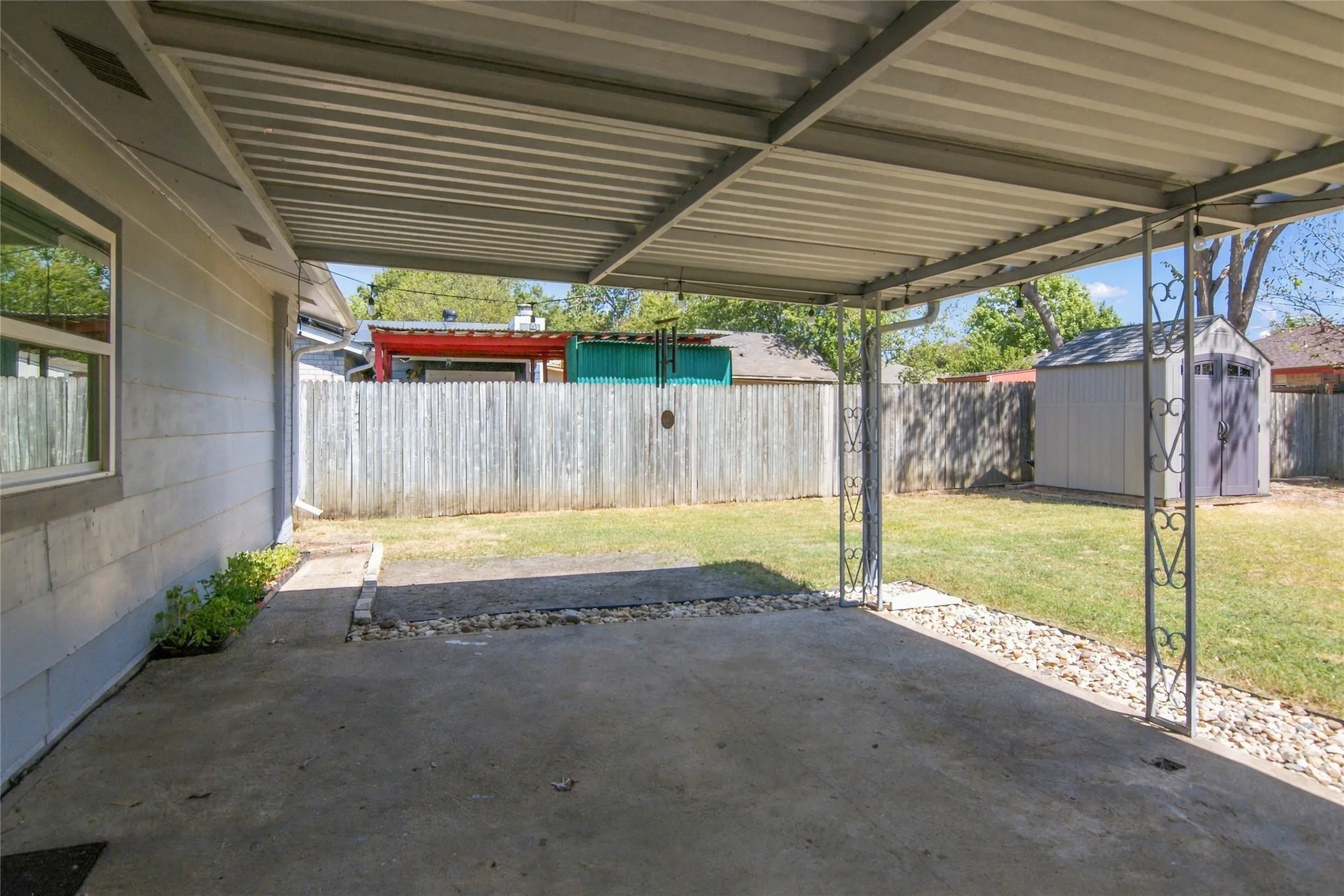 Covered patio with a concrete surface, metal support columns, and adjacent crushed stone landscaping