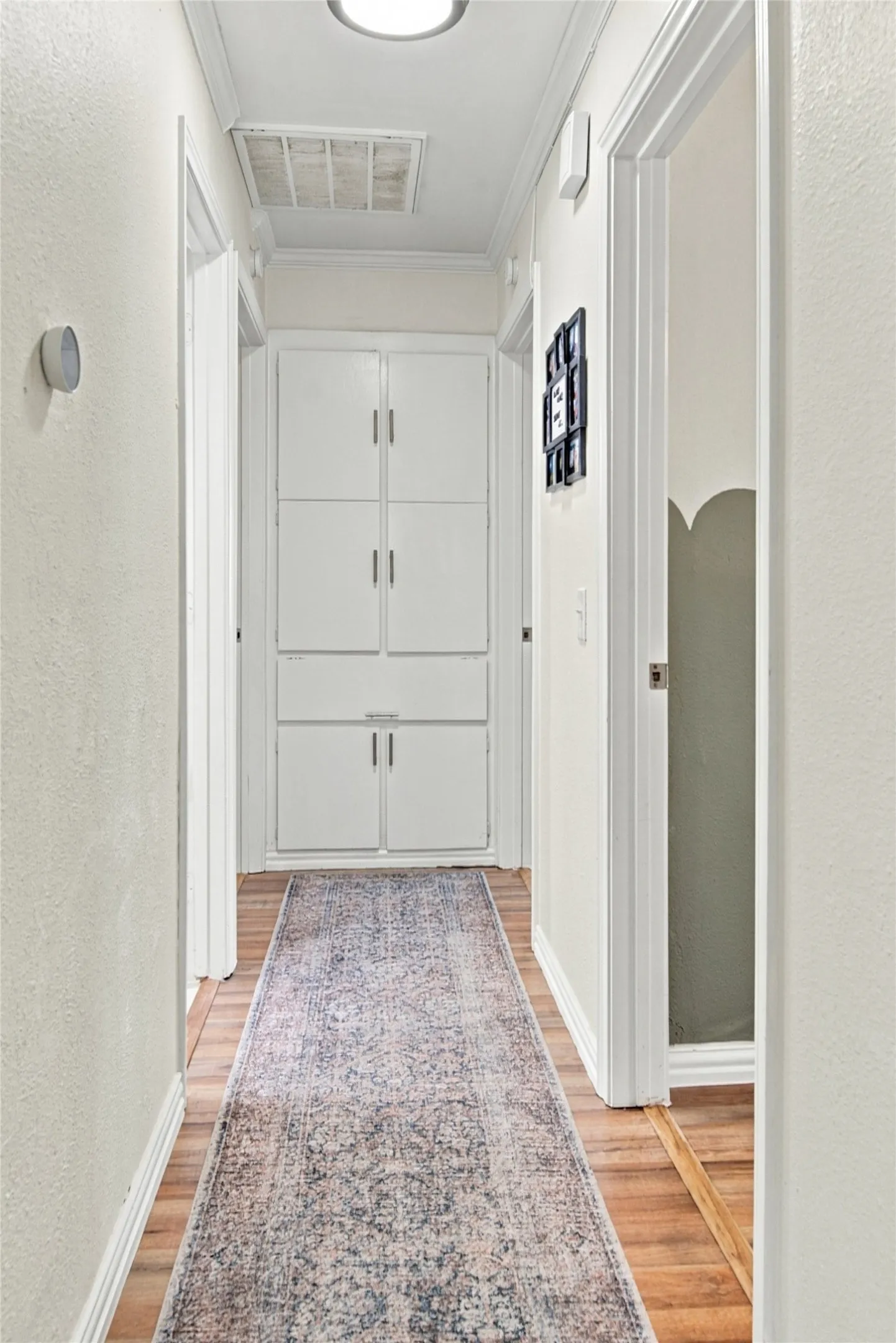 Wood-finish flooring throughout, featuring built-in white cabinetry, crown molding, and recessed lighting