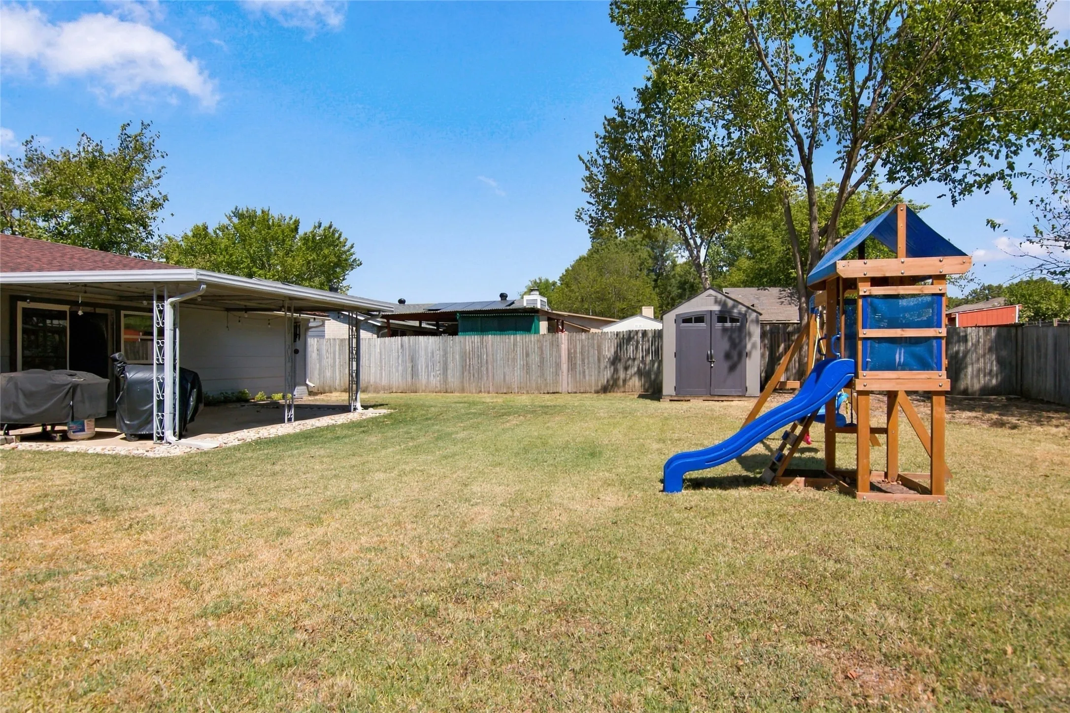 Expansive backyard featuring a covered patio, a manicured lawn, a privacy fence, and a storage shed