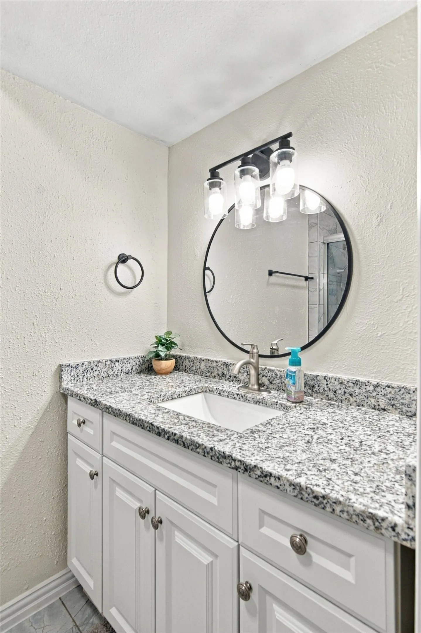 White vanity with paneled doors, speckled countertop, undermount sink, and brushed nickel faucet