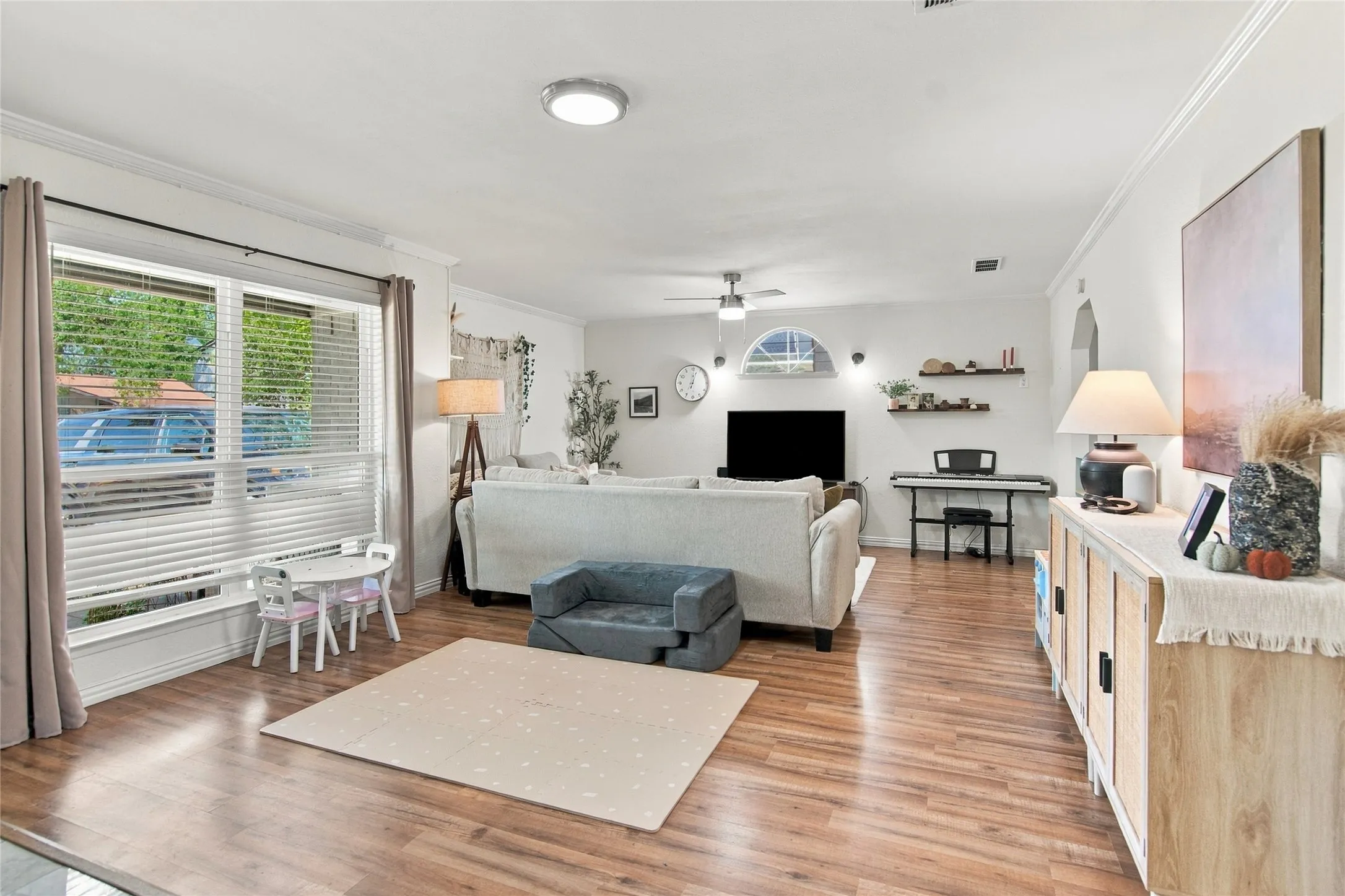 Wood-finish flooring, white walls, crown molding, a large window with blinds, and recessed lighting fixtures