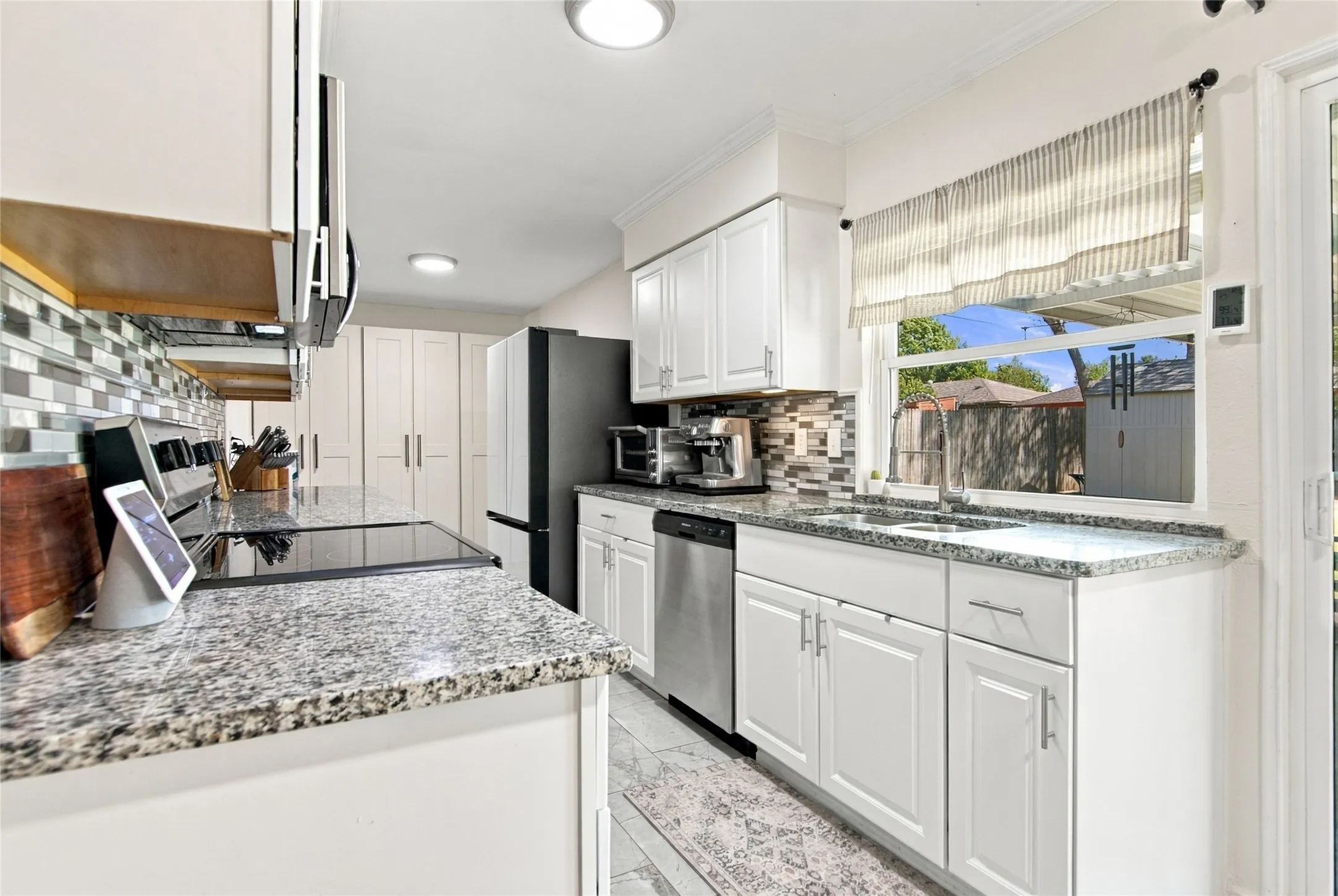 White cabinetry, speckled countertops, tile backsplash, stainless steel dishwasher, and a sliding glass door
