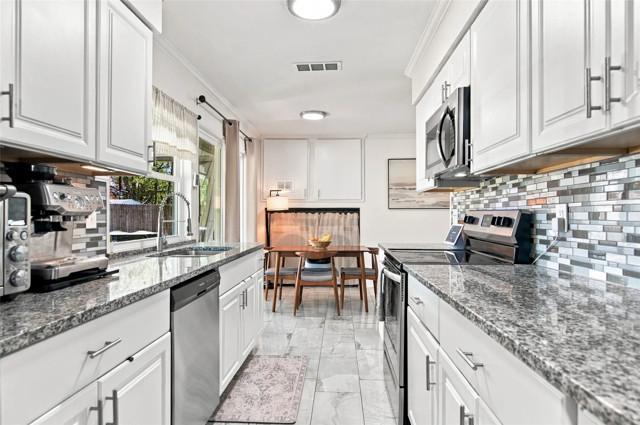 White cabinetry with brushed nickel hardware, granite countertops, stainless steel appliances, mosaic tile backsplash, and tile flooring