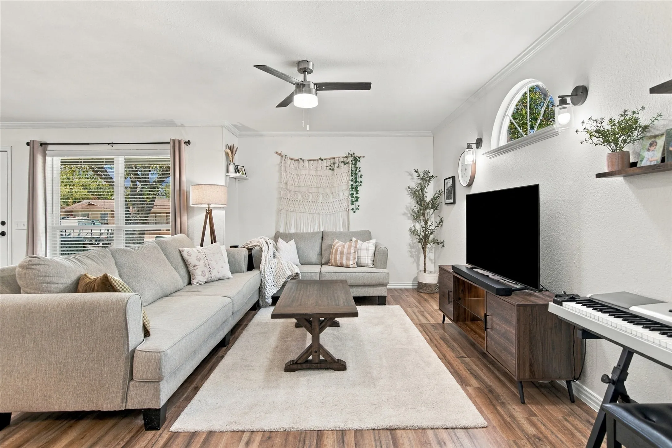 Wood-finish flooring, ceiling fan with integrated lighting, arched window, and recessed wall sconces
