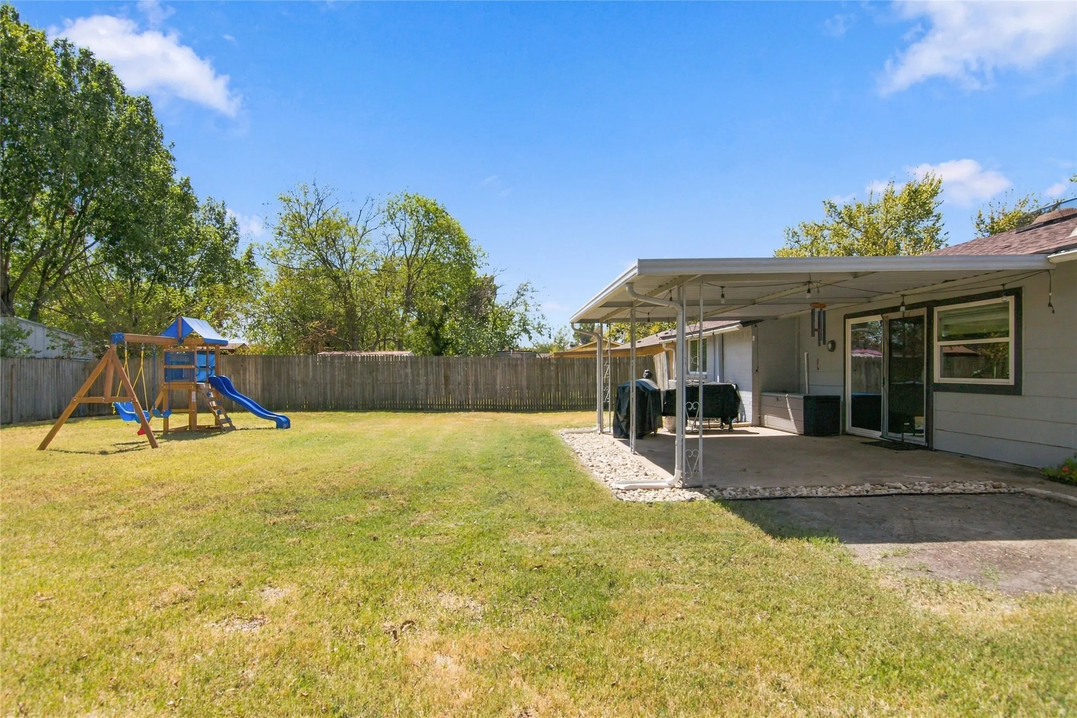 Expansive fenced yard featuring a covered patio with concrete flooring, a sliding glass door, and exterior windows
