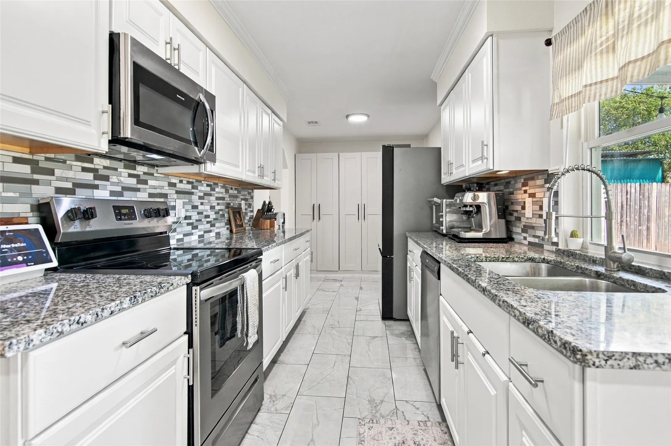 Galley kitchen featuring white cabinetry, granite-finish countertops, mosaic tile backsplash, and stainless steel appliances