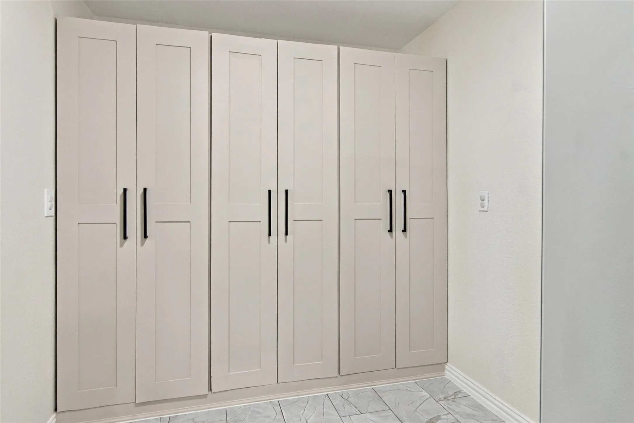 Built-in cabinetry with flat panel doors and matte black hardware, set against light-toned walls and patterned flooring