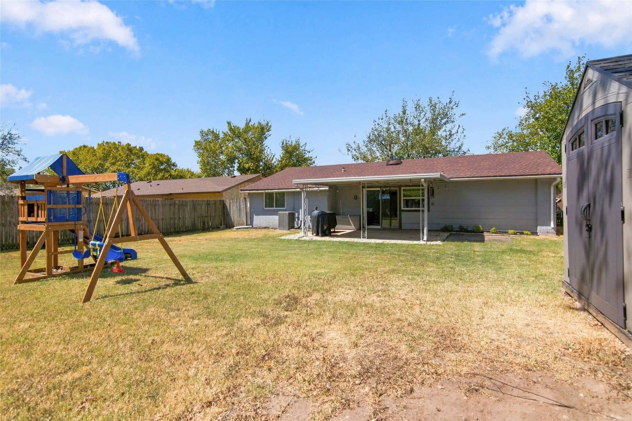 Expansive backyard featuring a covered patio, sliding glass door, and a storage shed
